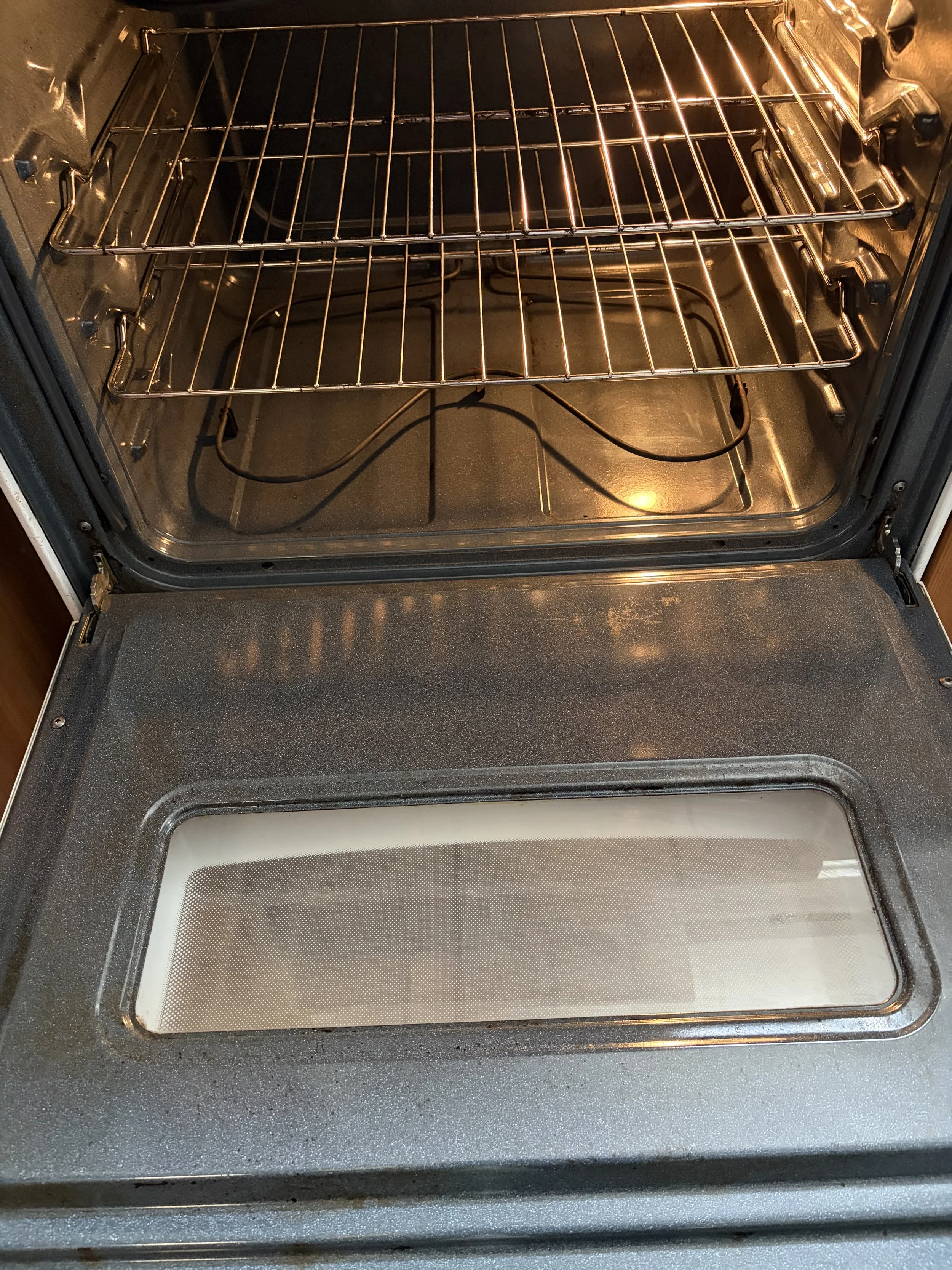 An open oven with two empty oven racks and a clean glass oven door.