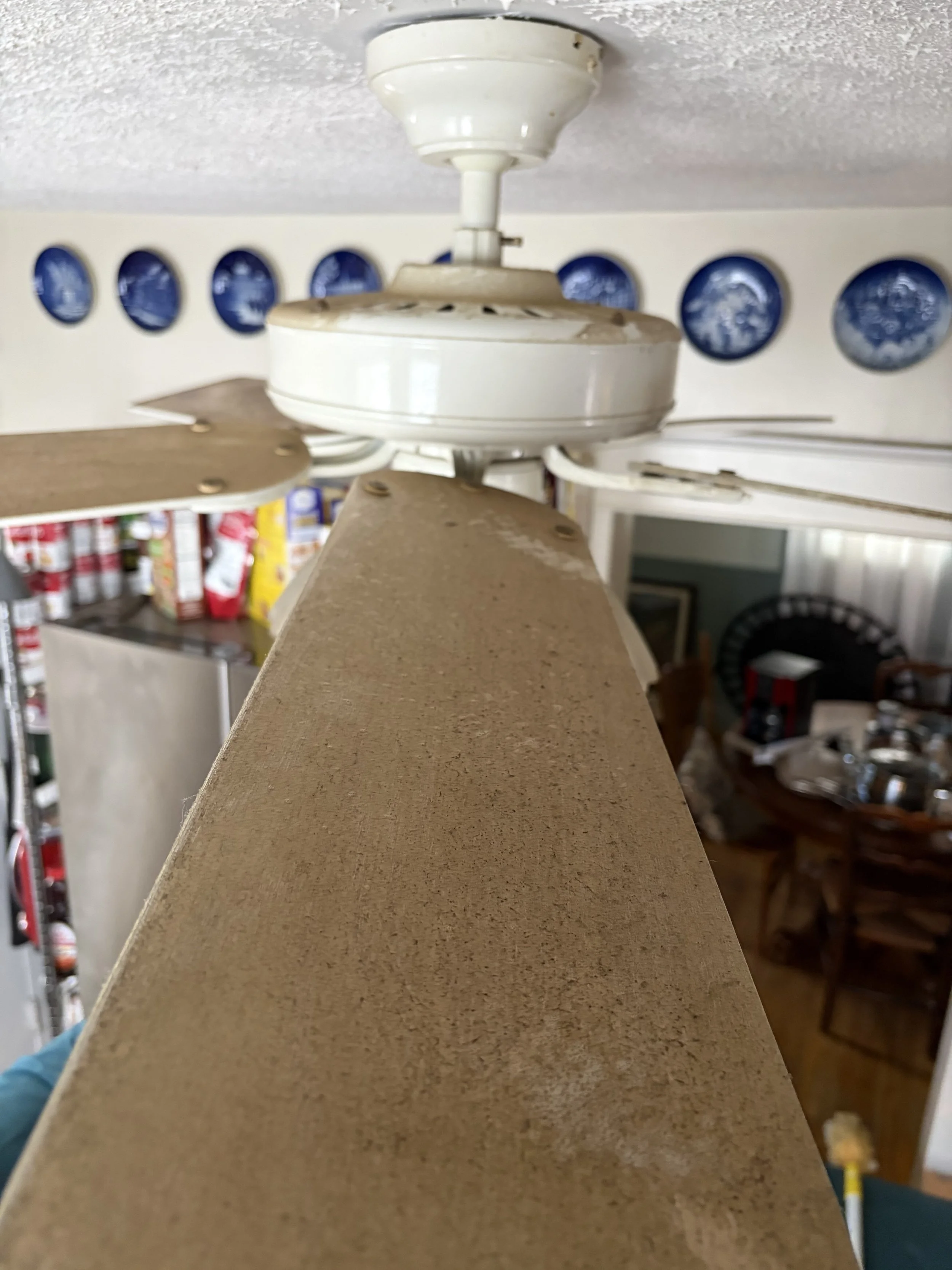 A dirty ceiling fan with blades mounted on a beige wall in a room.