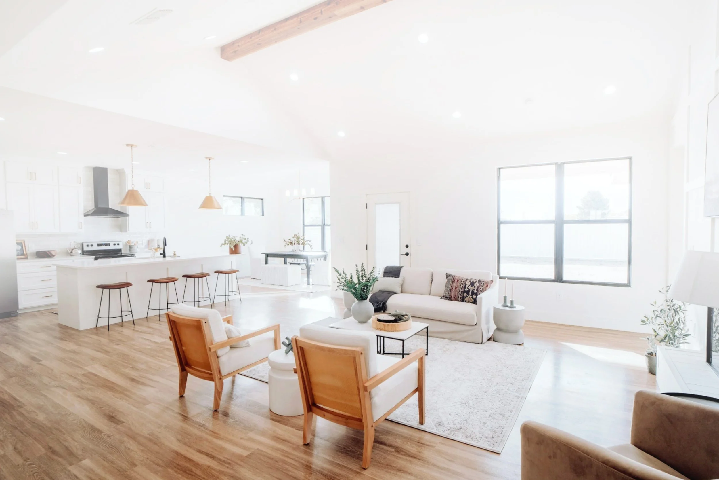 Freshly Clean, living space with a white kitchen, island, bar stools, and a cozy seating area with armchairs and a sofa. Large windows let in natural light, and hardwood floors add warmth in Frederick, Maryland