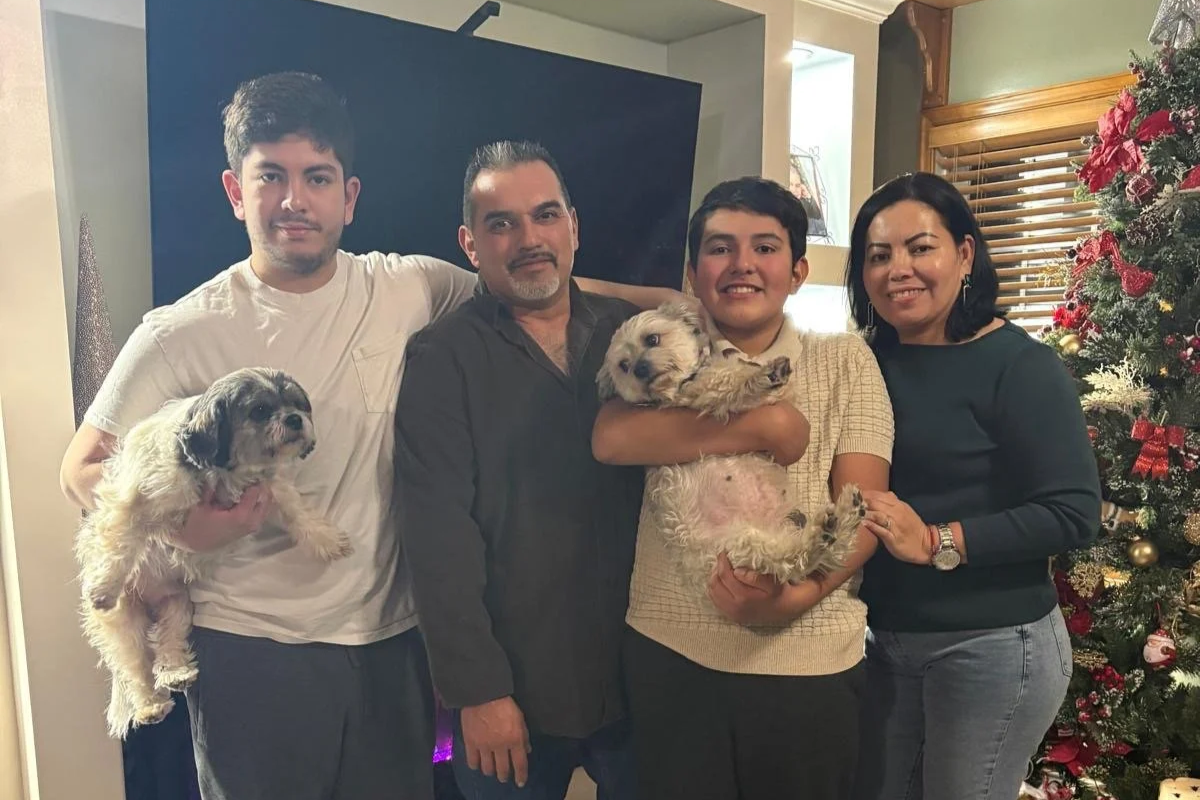 A family of five with two dogs celebrating Christmas, standing near a decorated Christmas tree in a cozy living room.