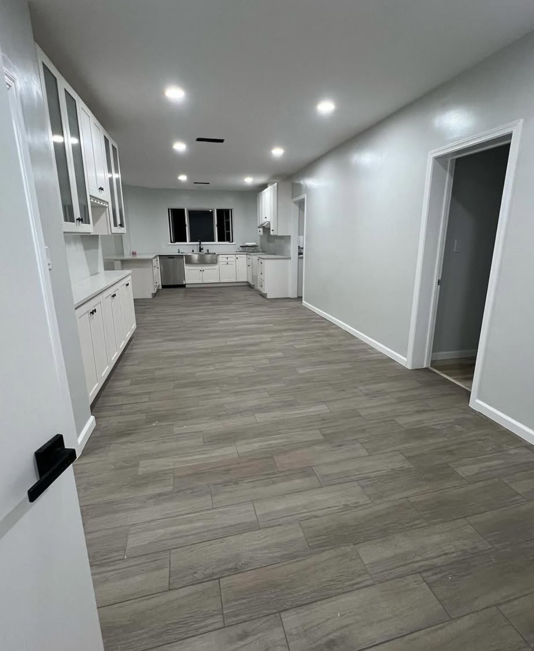 Full kitchen and interior remodel by Repairs y More featuring clean white cabinets, grey wood-look flooring, stainless steel appliances, and bright modern finishes in a Los Angeles County home.