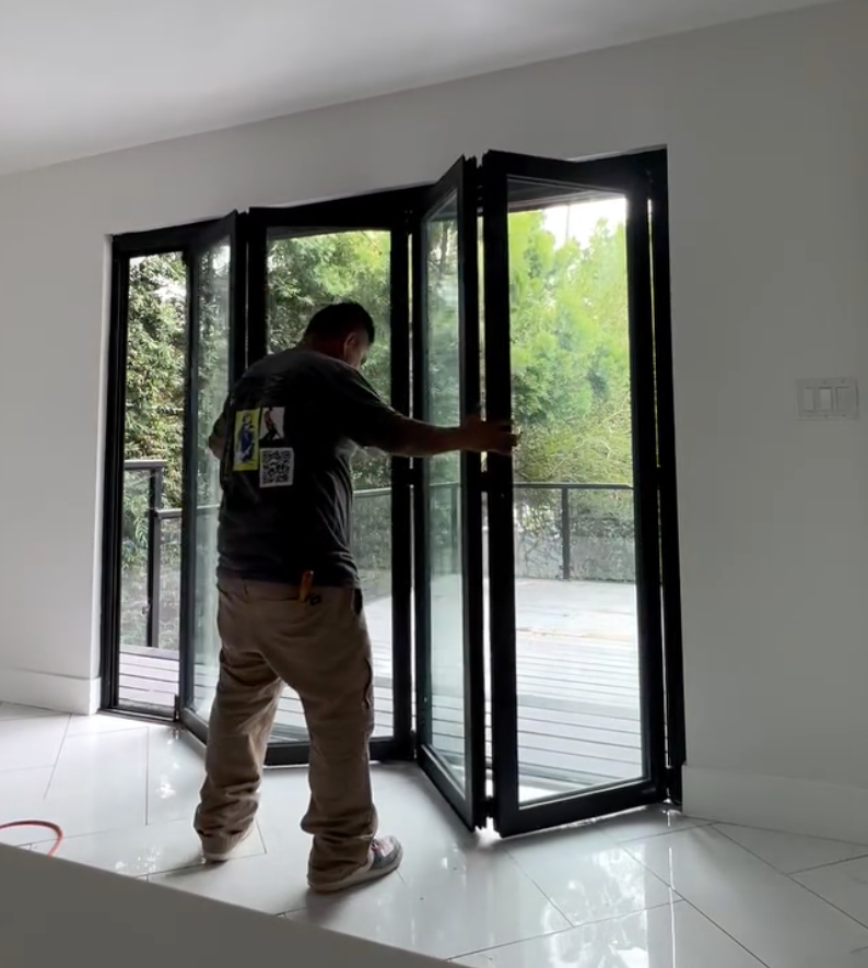 Installation of black bifold glass doors by Repairs y More, creating a seamless indoor-outdoor connection with a large opening to the backyard deck in a Los Angeles area home.