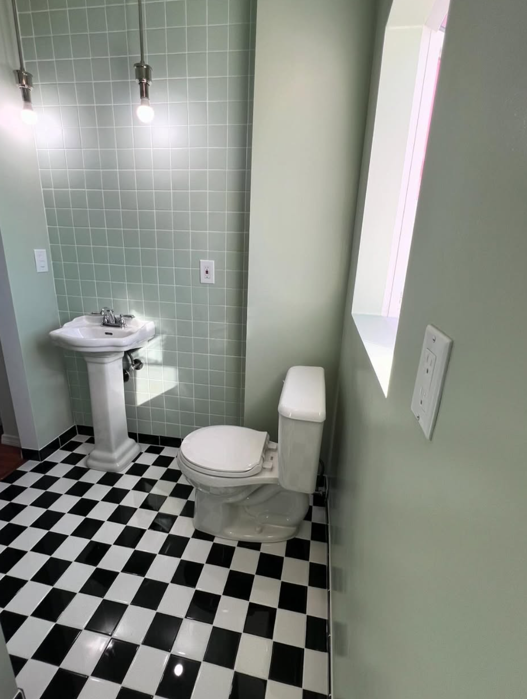 Retro-style bathroom renovation by Repairs y More featuring classic black and white checkerboard tile flooring, mint green subway tile walls, and a vintage pedestal sink in a Los Angeles area home.