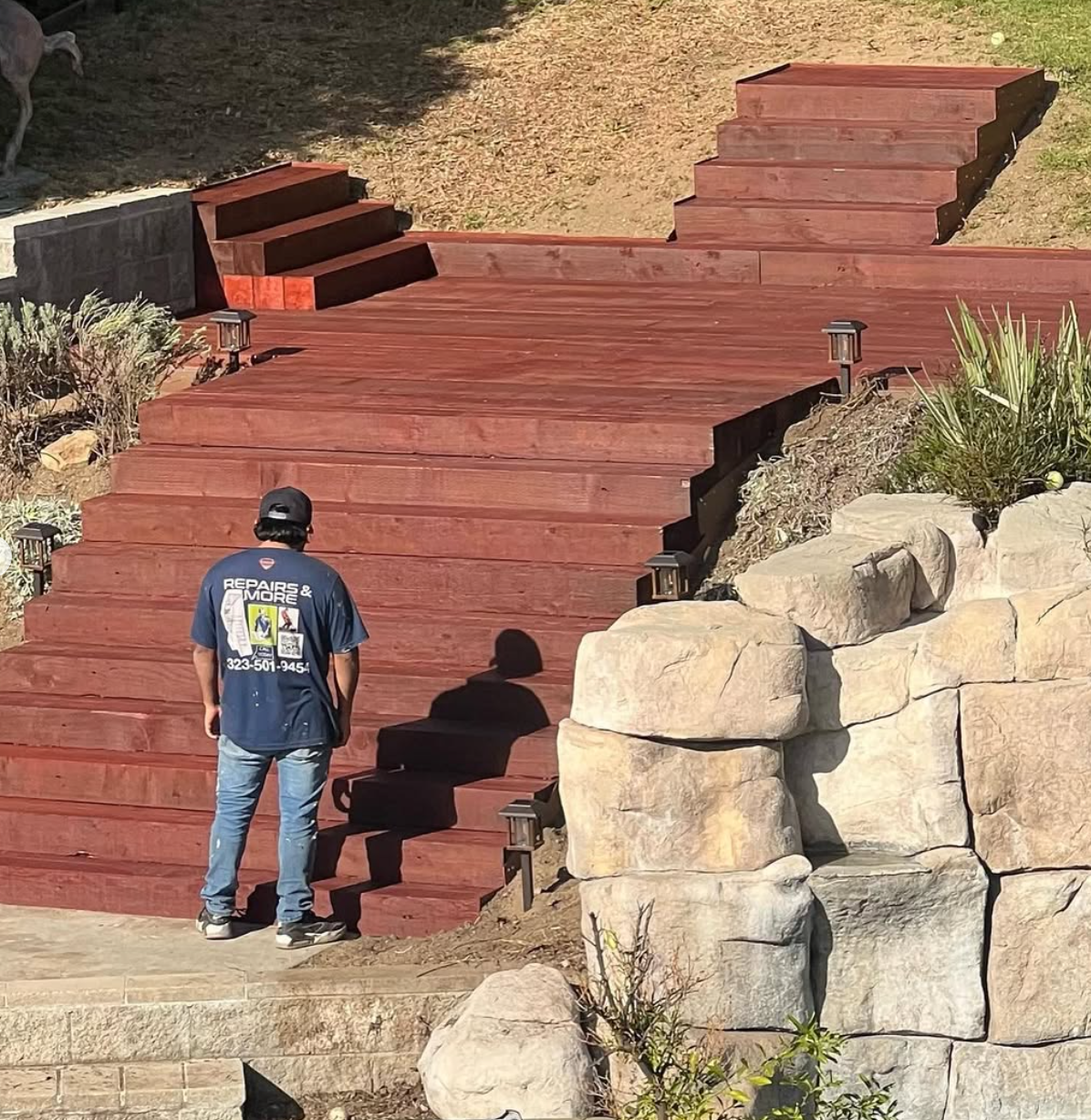 Custom multi-level redwood deck and stairs built by Repairs y More on a sloped hillside, featuring integrated lighting and natural stone retaining walls in a Los Angeles area backyard.