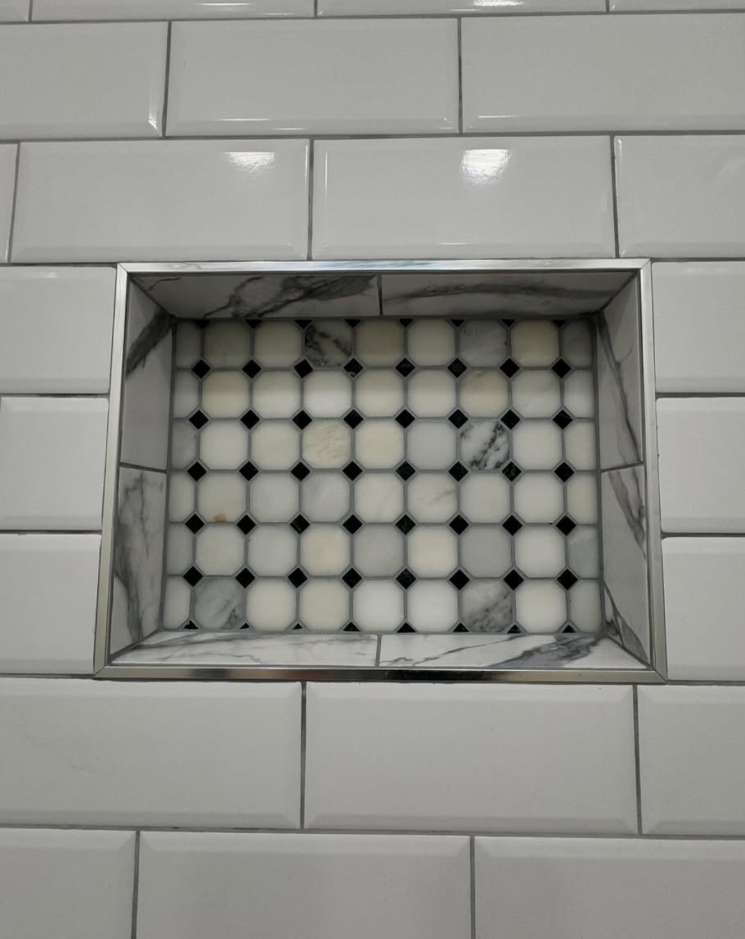 Custom recessed shower niche with marble hexagon tile detail by Repairs y More, framed in polished chrome and set into a clean white subway tile wall.