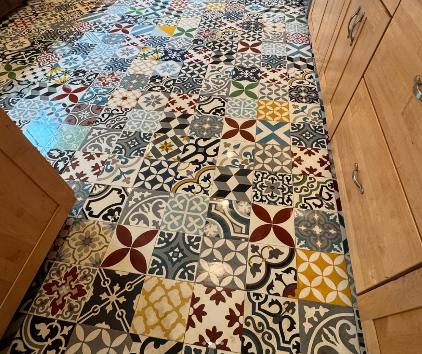 Colorful patterned tile flooring installed by Repairs y More in a kitchen remodel. Vibrant mix of decorative tiles creates a bold, artistic look with light wood cabinets.
