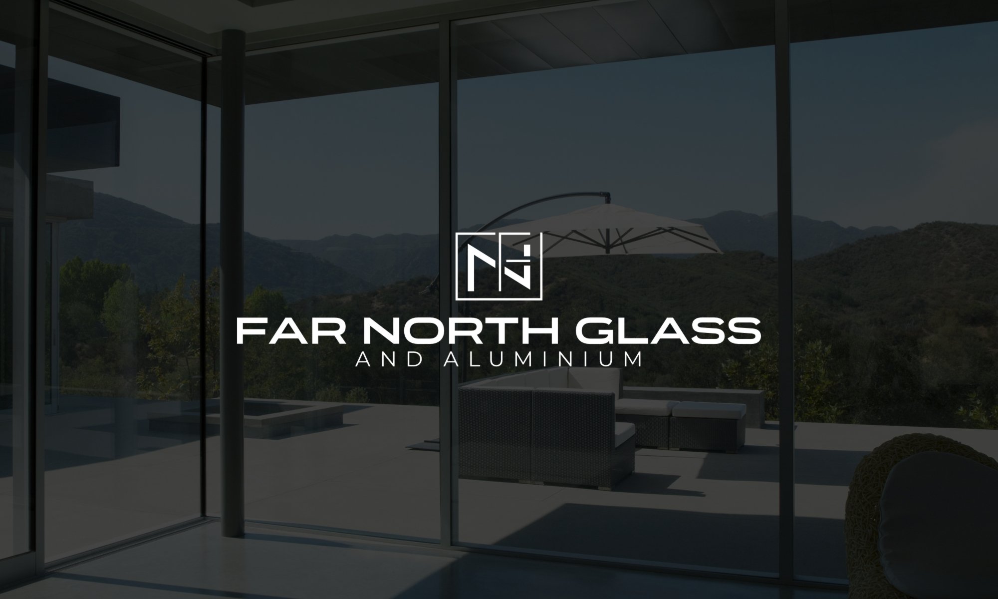 Modern glass house with outdoor seating and view of mountains and trees.