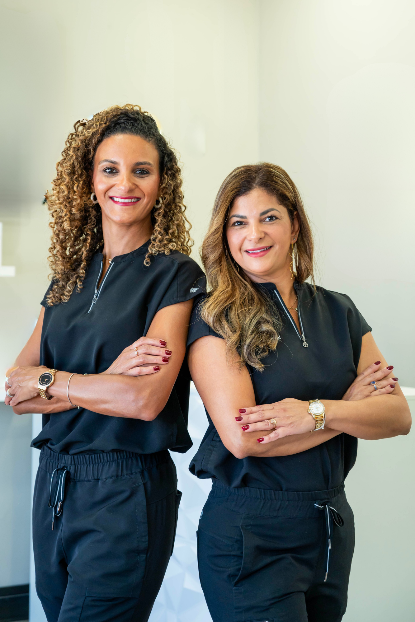 Two women in black athletic outfits stand with arms crossed, smiling confidently in a bright indoor space.