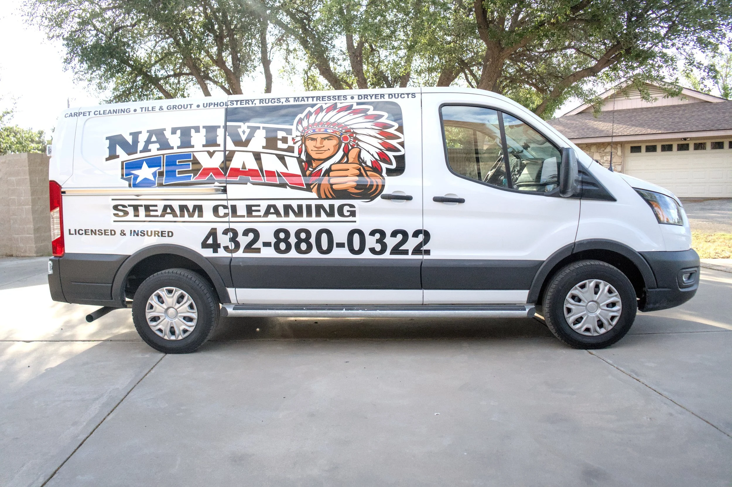 White service van with colorful logo and text for Nate Van Steam Cleaning parked in front of a house and trees.