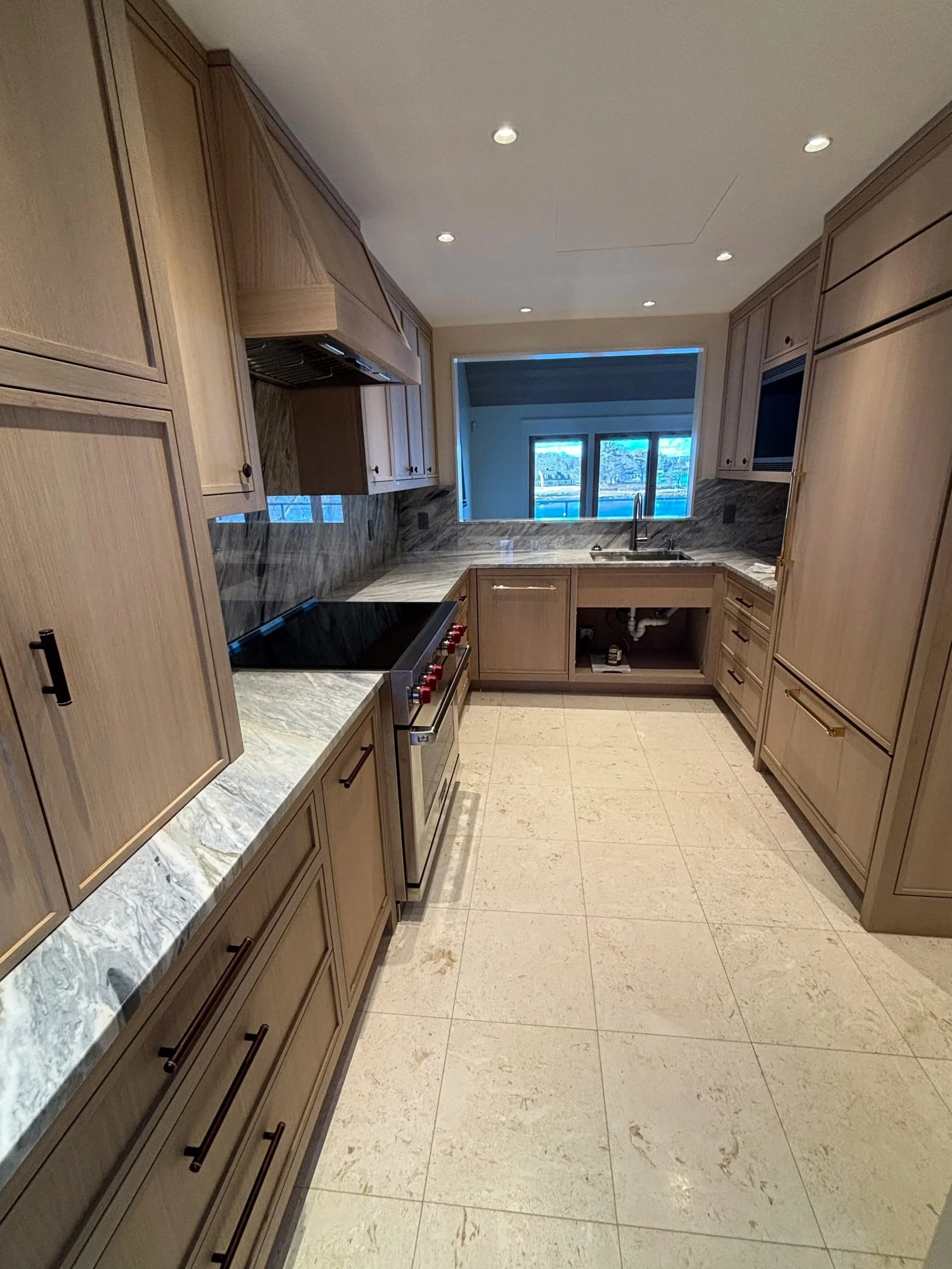Kitchen with wooden cabinets, marble countertops, a window above the sink, and tiled floor.