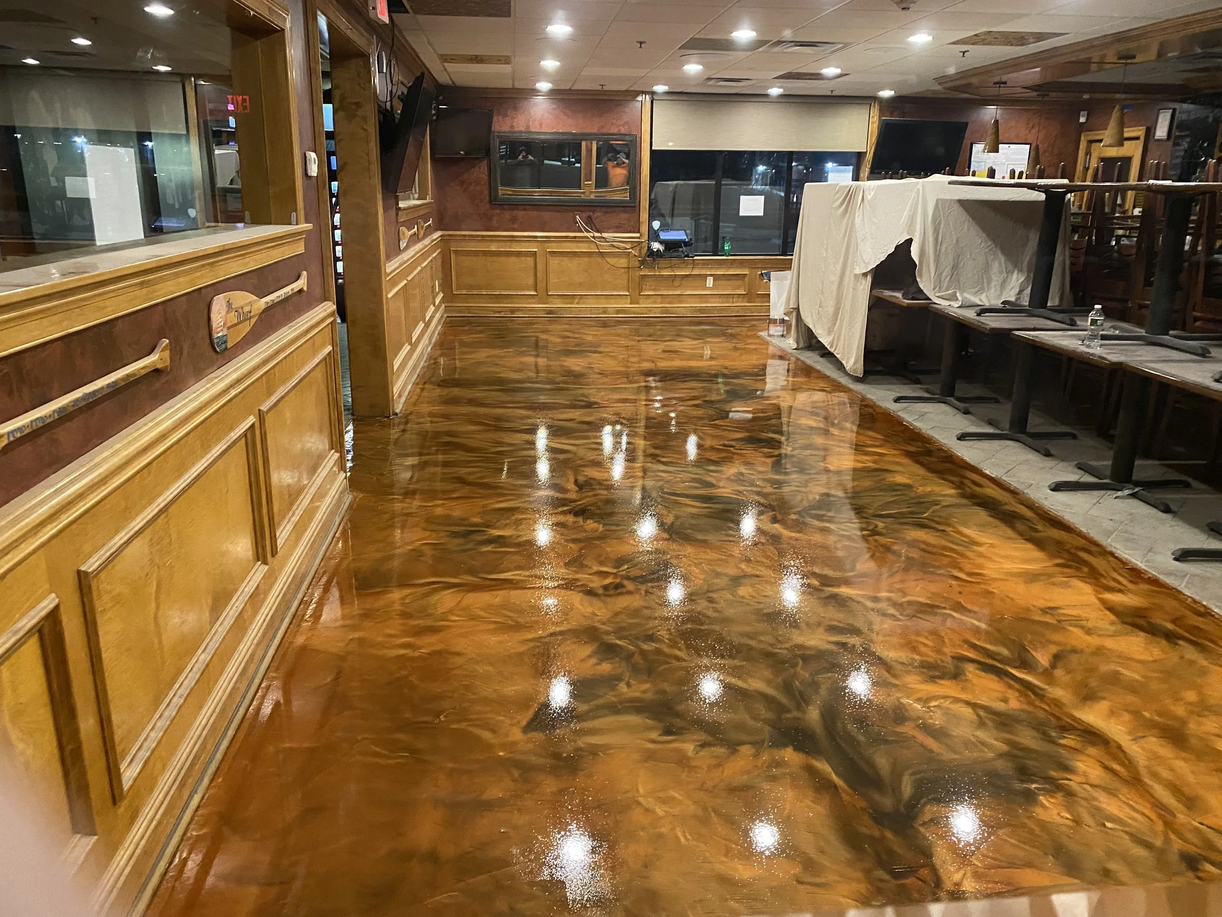 An empty restaurant with a polished wooden floor, a wrapped table, wall-mounted TV, and large windows.