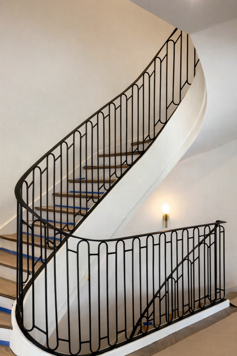 Interior view of a curved staircase with iron railings and wooden steps, partially under construction or renovation.