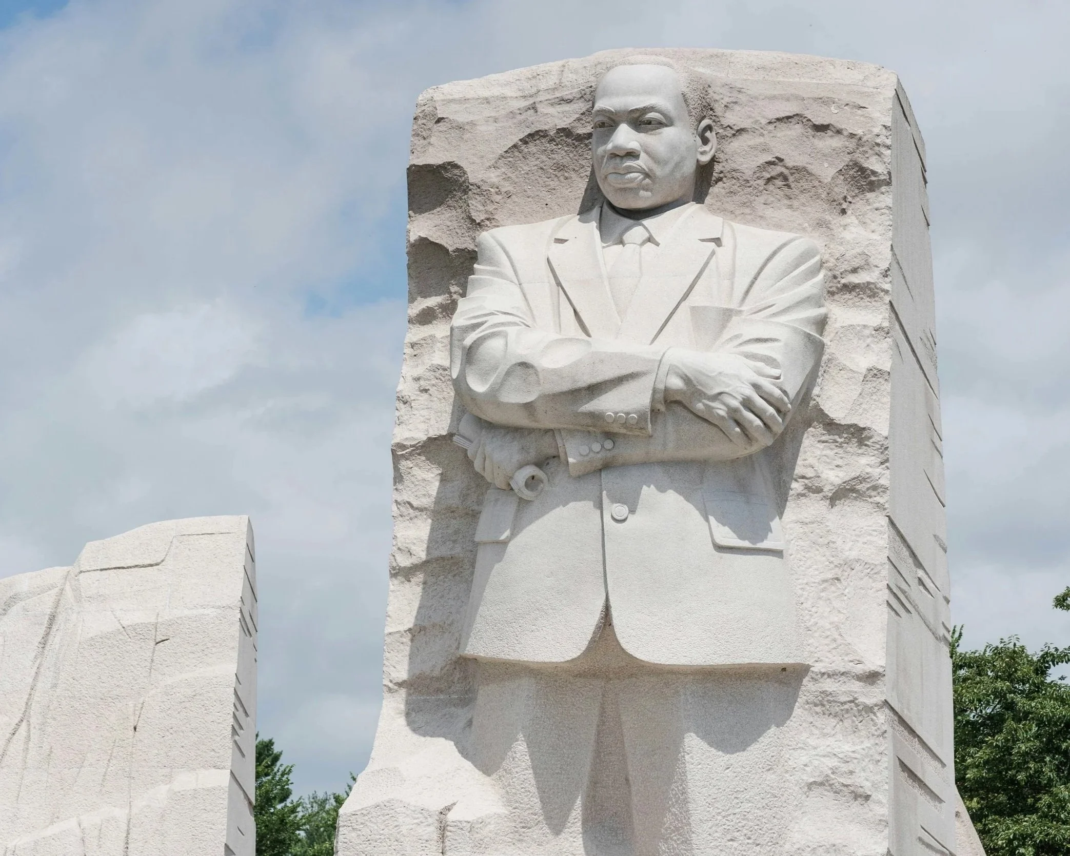The Lincoln Memorial statue of Abraham Lincoln carved from white marble, with arms crossed, wearing a suit, against a partly cloudy sky.