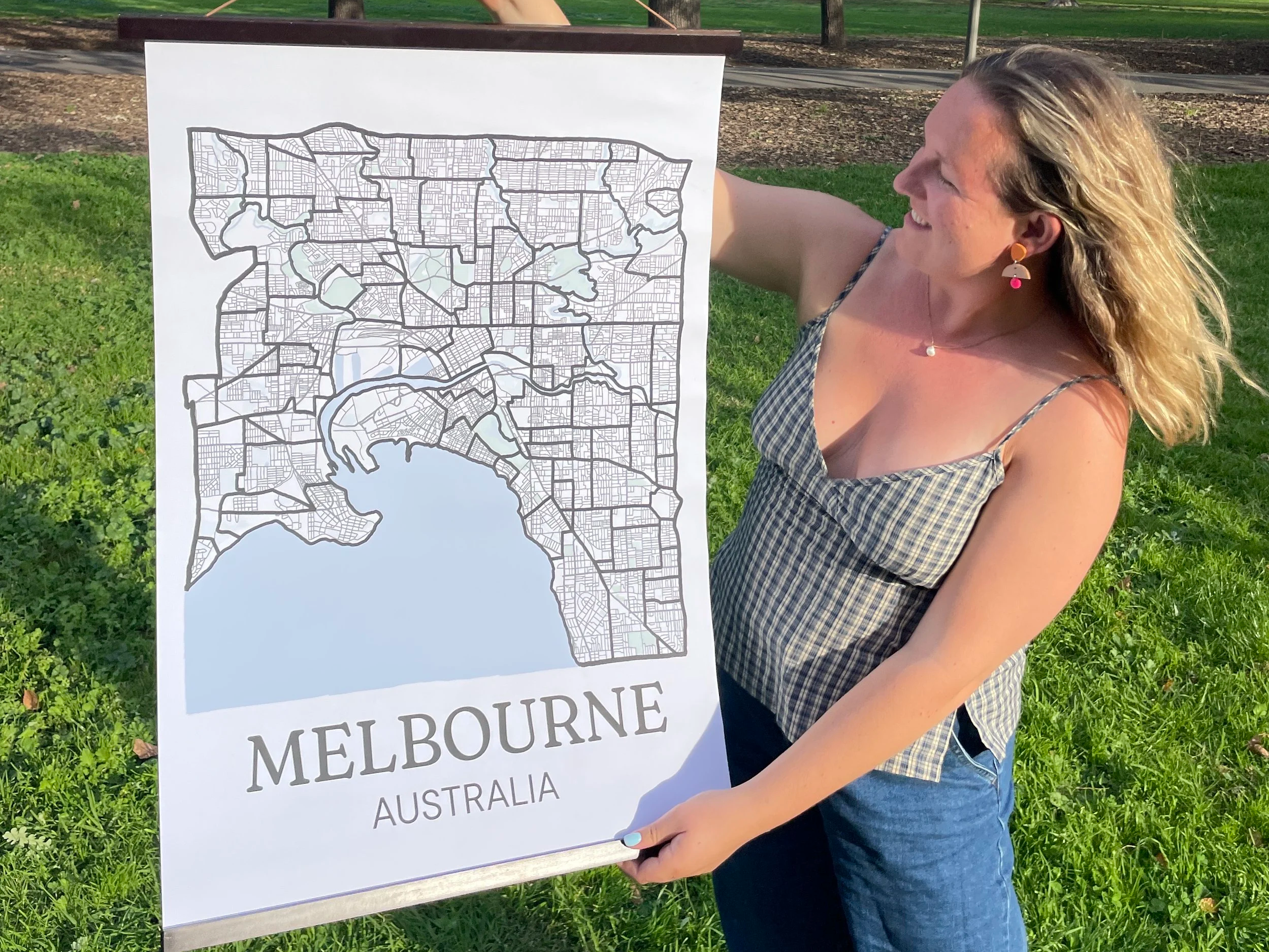 Painting by Suburbs founder holding up a large Melbourne suburb map poster with a wooden hanger frame in an outdoor park setting