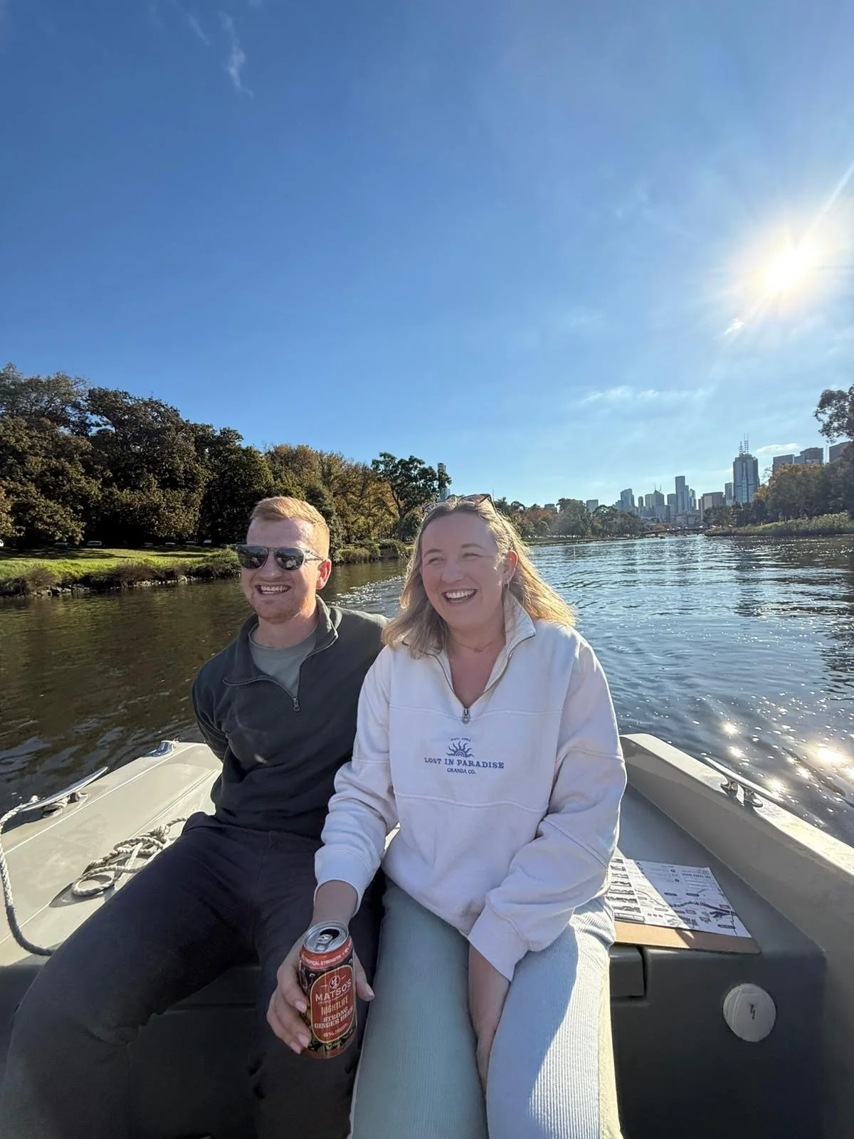 Painting by Suburbs founder and her partner smiling on a boat on the Yarra River with the Melbourne skyline behind them, the date night that inspired the idea to explore Melbourne suburb by suburb