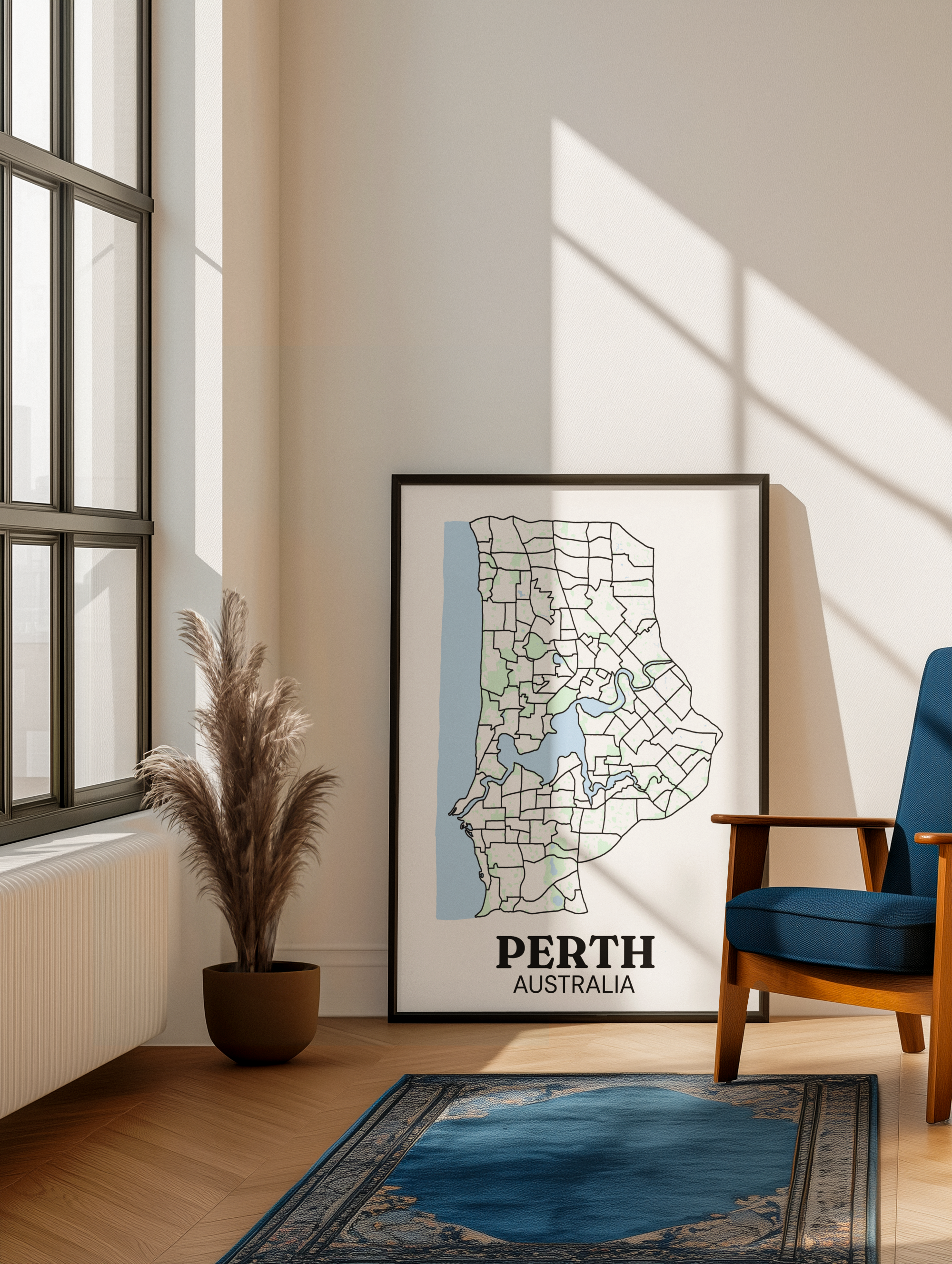 Black-framed suburb boundary map print of Perth, Australia leaning against a wall in a sunlit living room with a pampas grass plant and blue Persian rug.