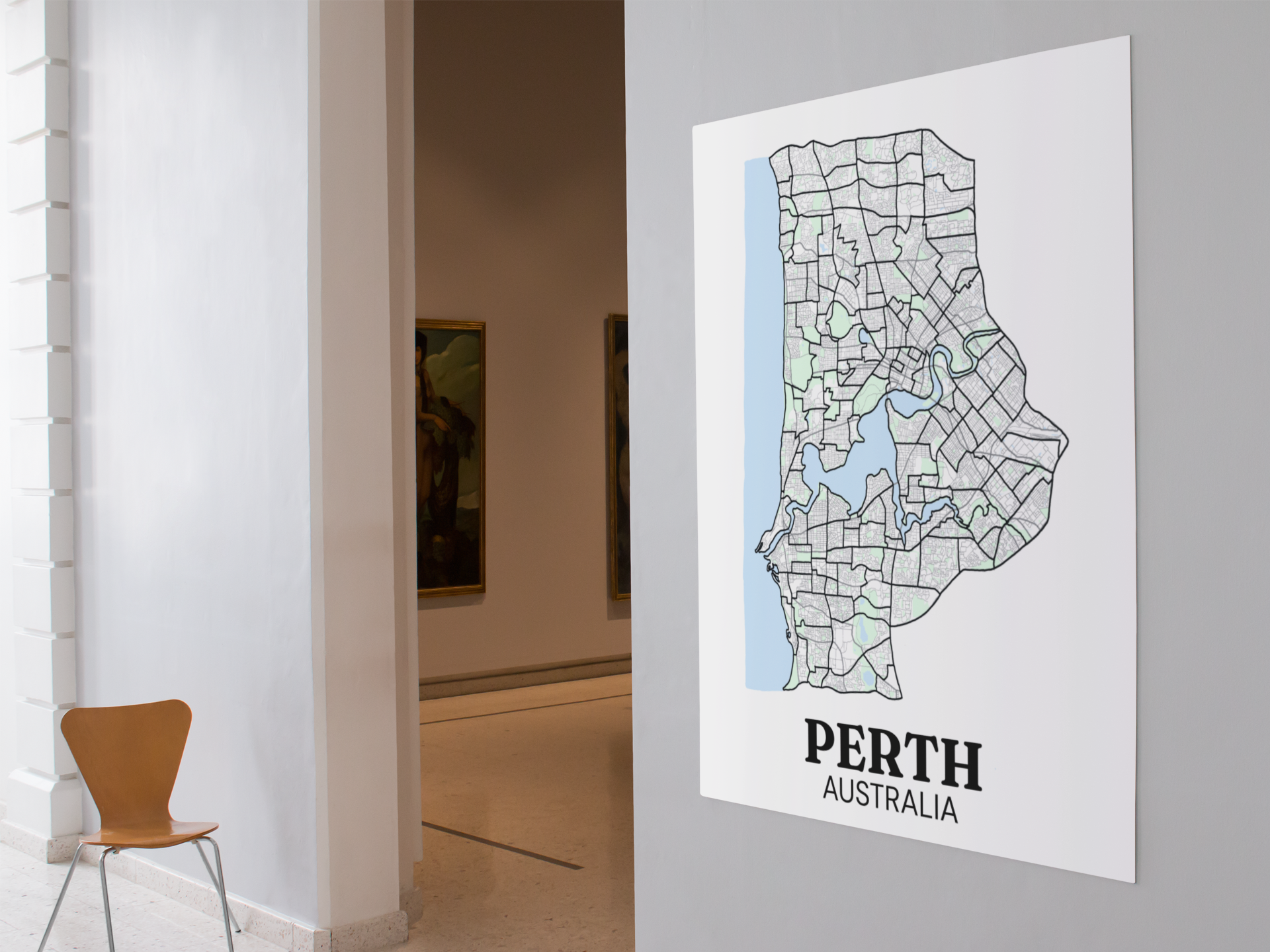 Unframed colour street map poster of Perth, Australia displayed on a gallery wall beside an open doorway with framed paintings visible.