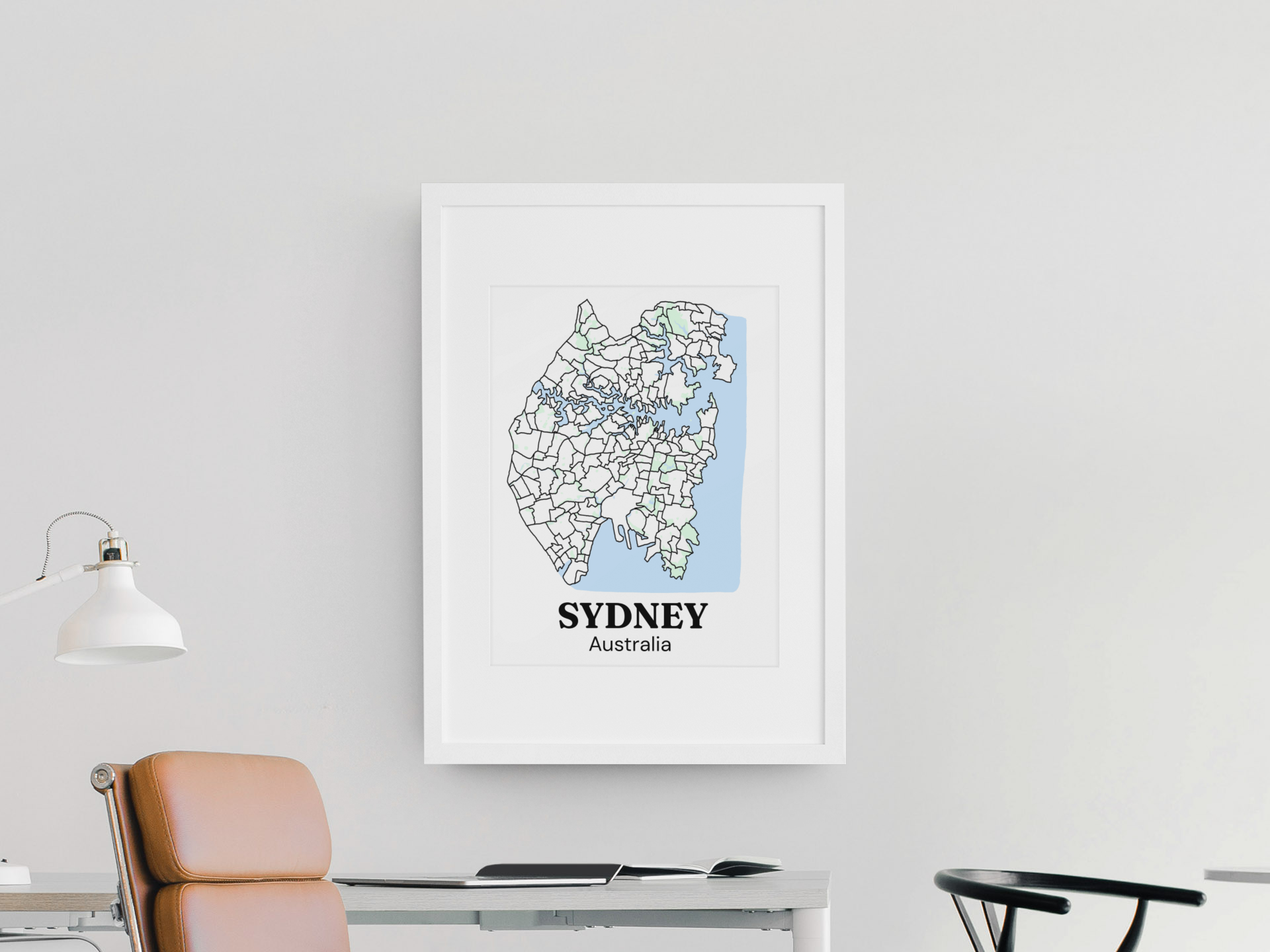 White-framed bare Sydney suburb map print hanging above a modern desk with a leather chair, in a minimalist office setting