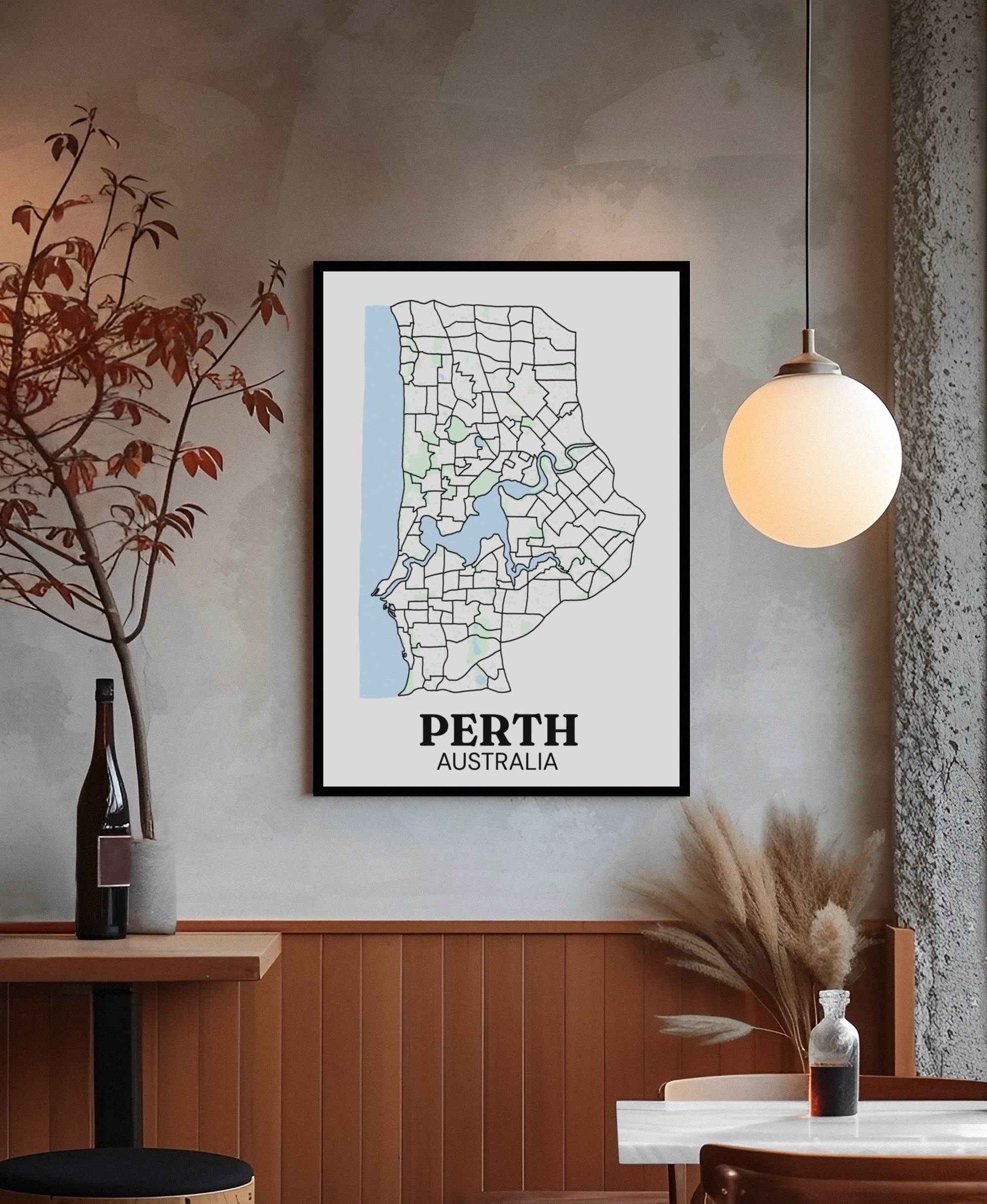 Black-framed suburb boundary map print of Perth, Australia hung on a textured wall beside a globe pendant light and dried branches.
