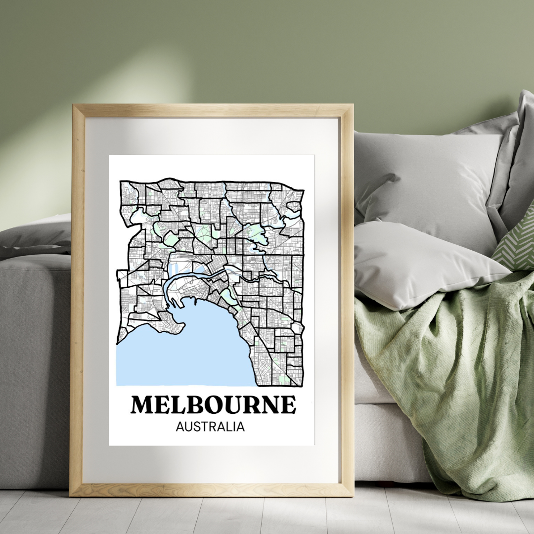 Framed Melbourne suburb map print leaning against a sofa in a green and grey living room, showing the blank unpainted design ready to be filled in as suburbs are explored.