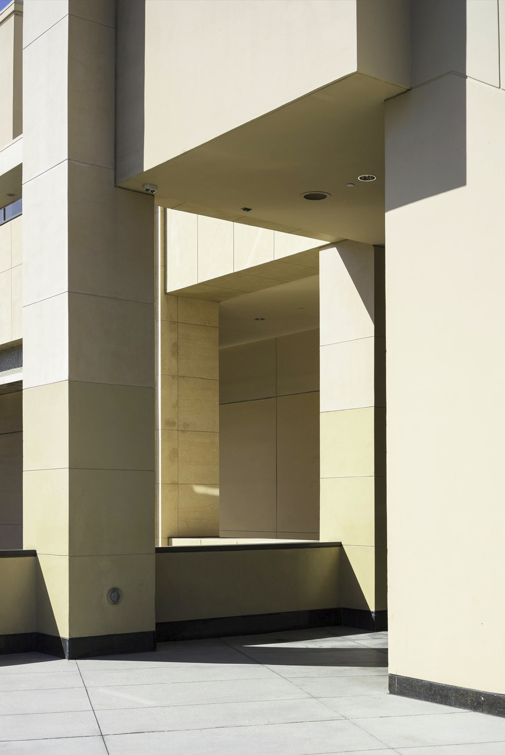 Modern beige and cream-colored building exterior with geometric design and shadows, featuring a small round security camera.