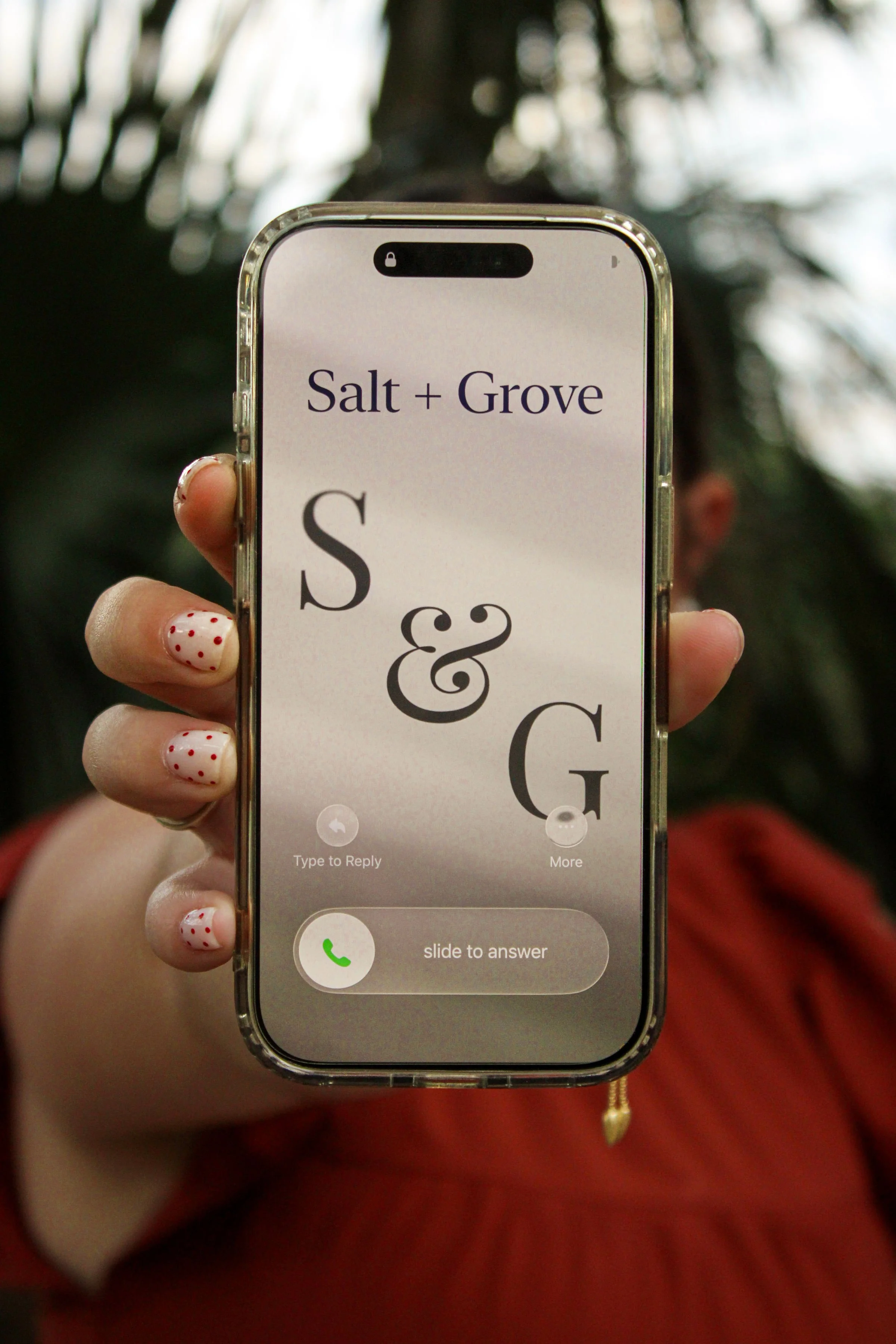 A person with polka dot painted nails holding a smartphone displaying a caller screen with 'Salt + Grove' as the caller and the initials 'S & G' in large font.
