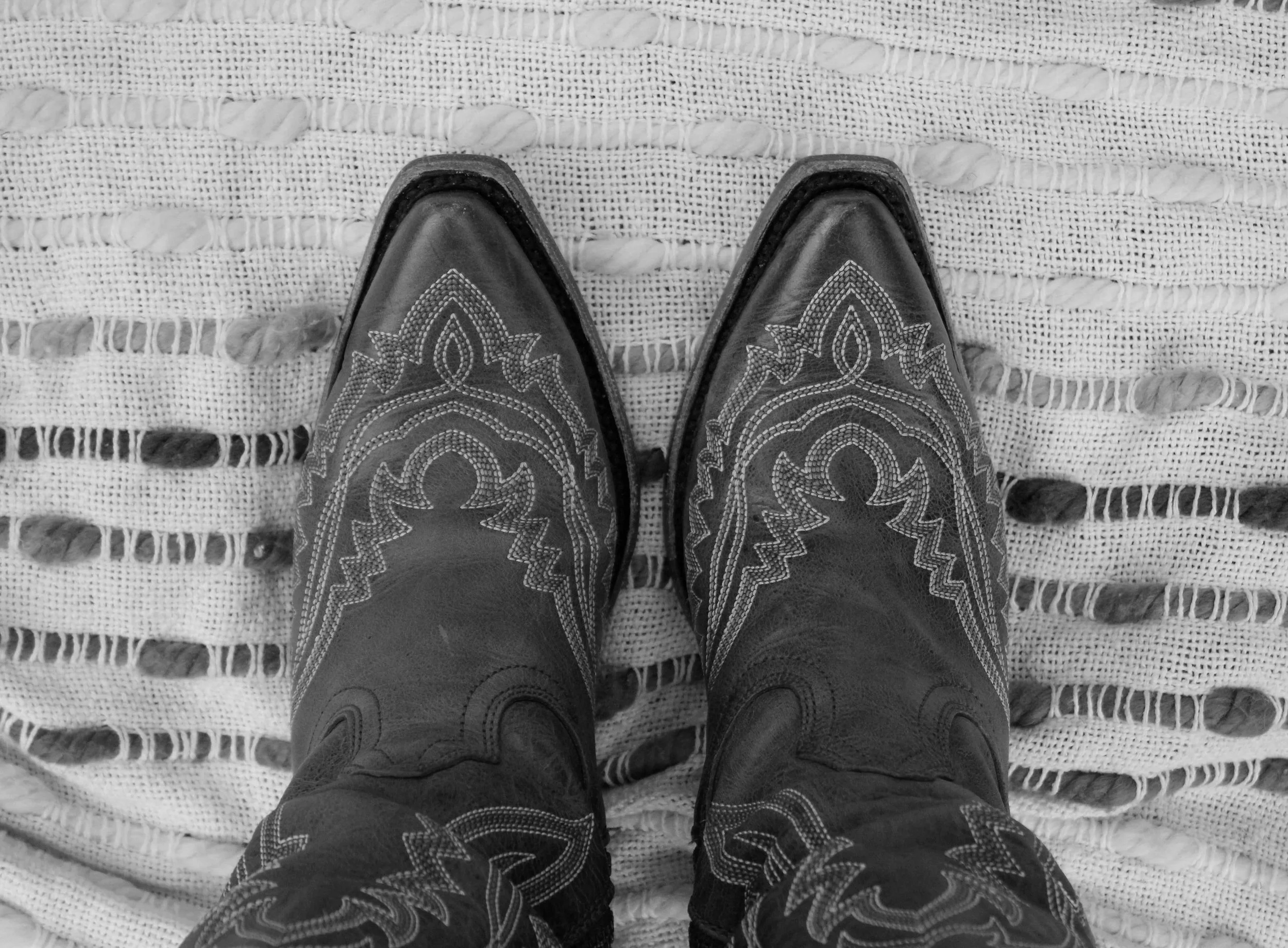 Black cowboy boots with decorative stitching on a white woven rug.