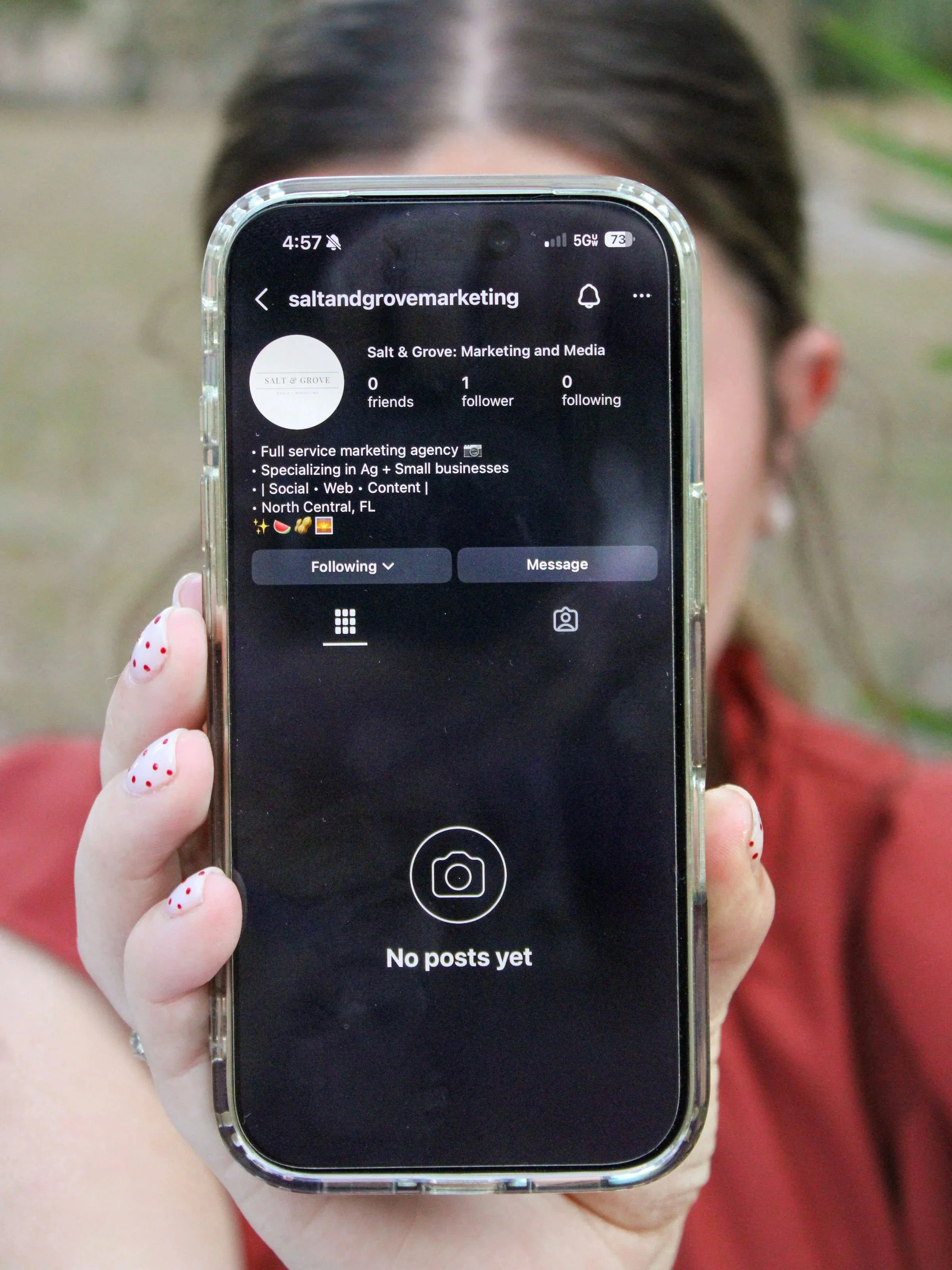 A person holding a smartphone in front of their face, showing a social media profile for 'saltandgrovemarkteting' with no posts yet.