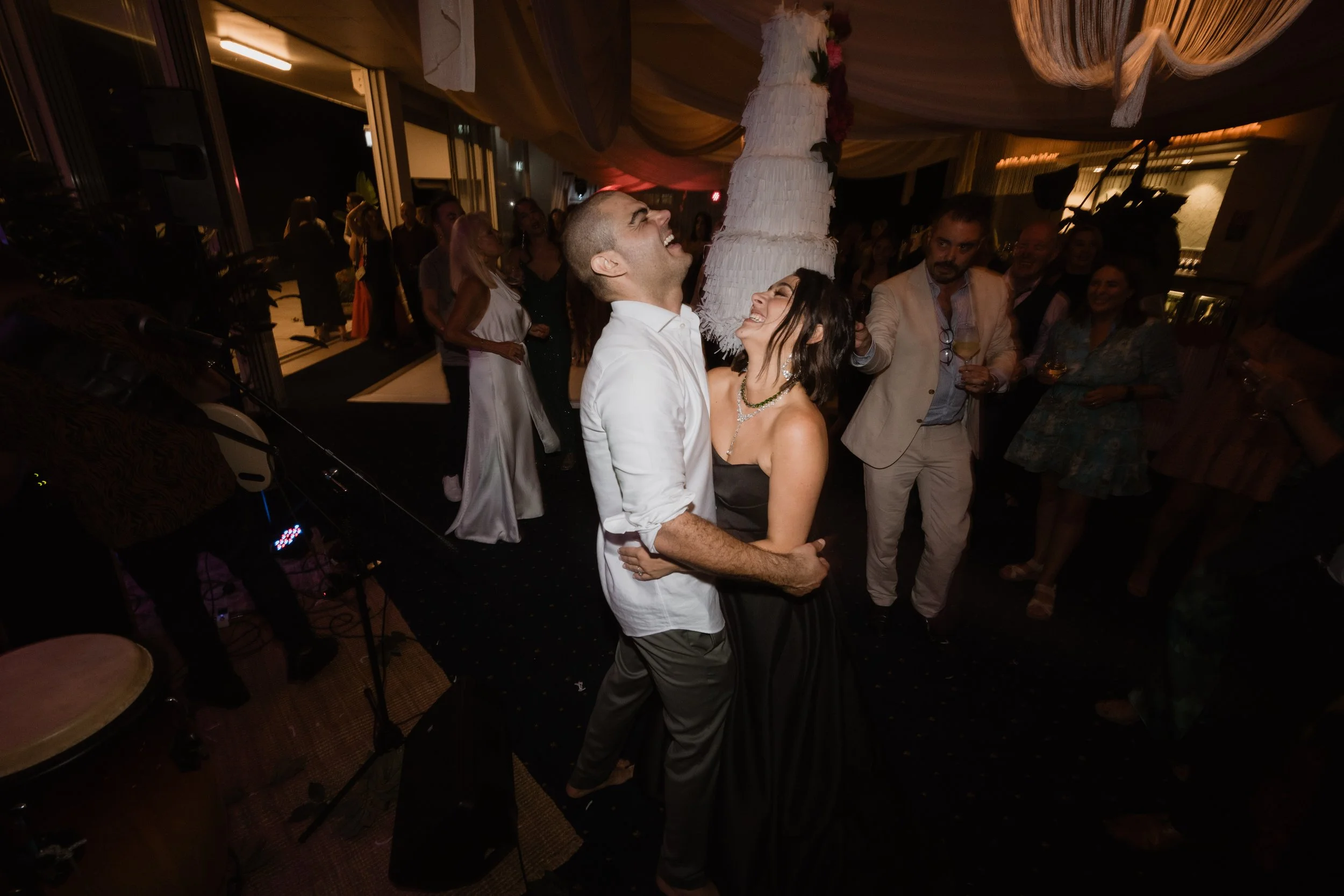 A couple dancing closely at a wedding reception with guests in the background.