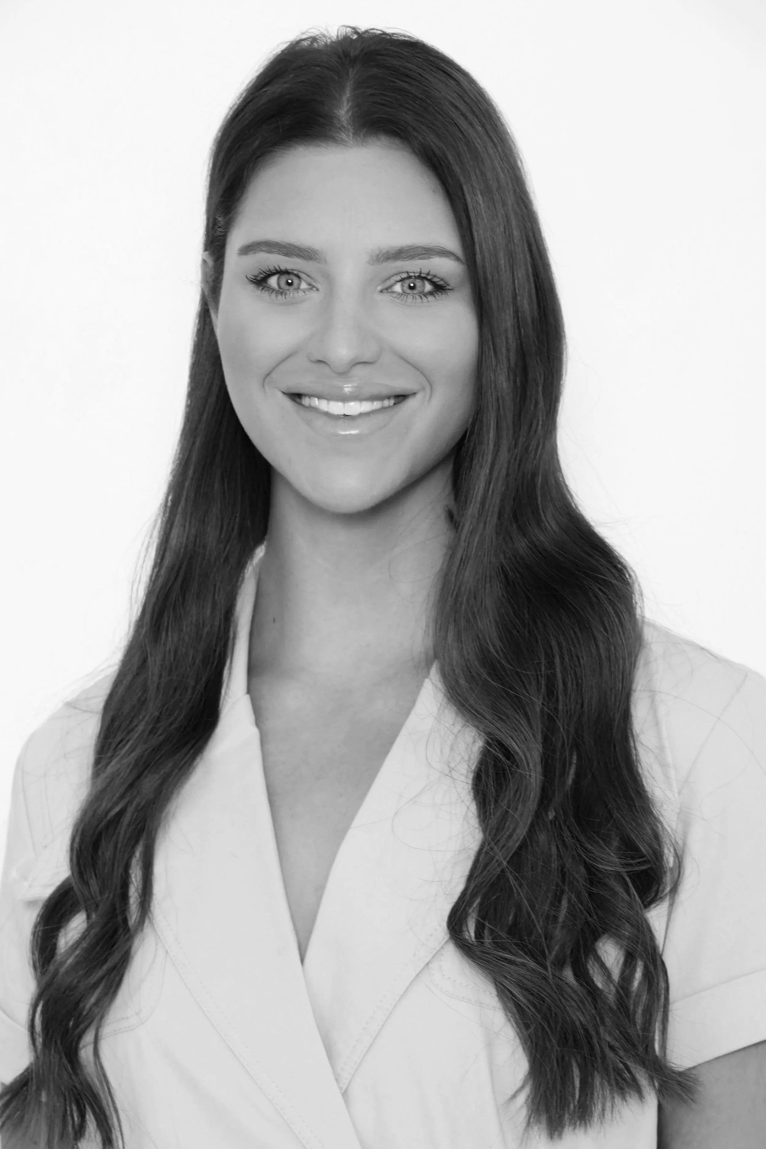 Black and white portrait of a woman with long wavy hair, smiling, wearing a V-neck top.