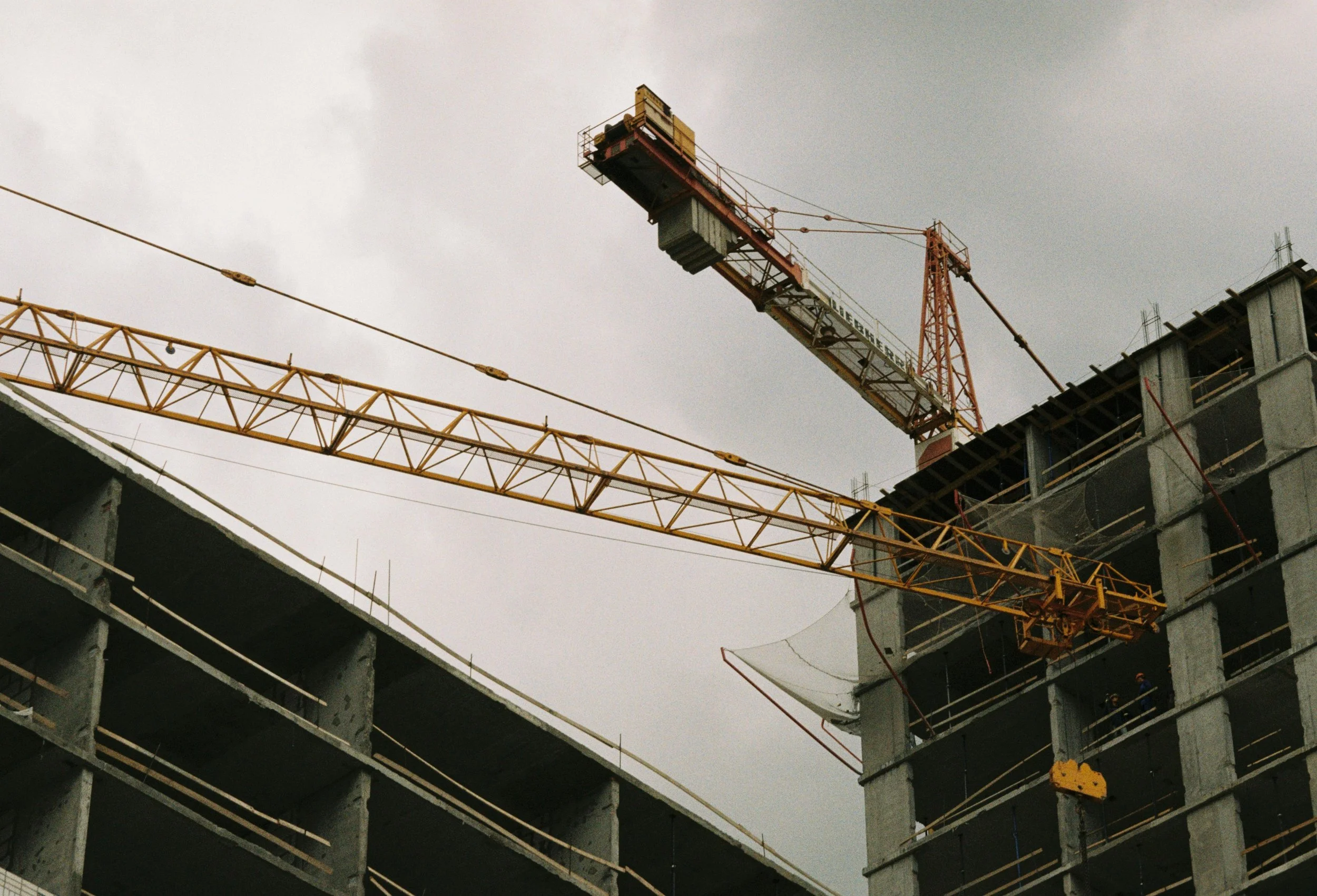 Construction site with a large tower crane and partially built concrete structures under a cloudy sky.