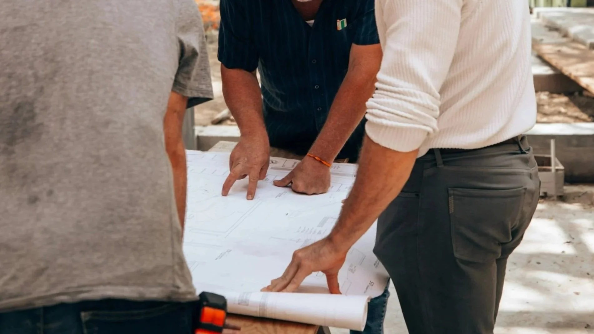 Group of people examining blueprints or plans at a construction site.