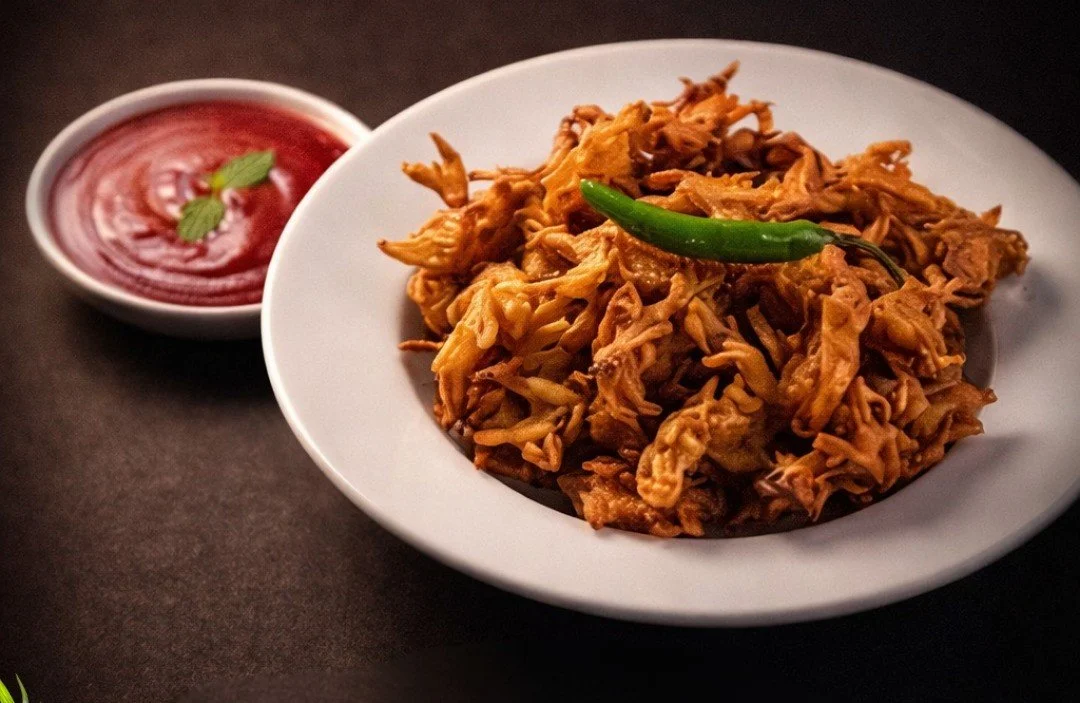 A plate of shredded chicken with a green chili on top, served with a small bowl of red sauce garnished with mint leaves.
