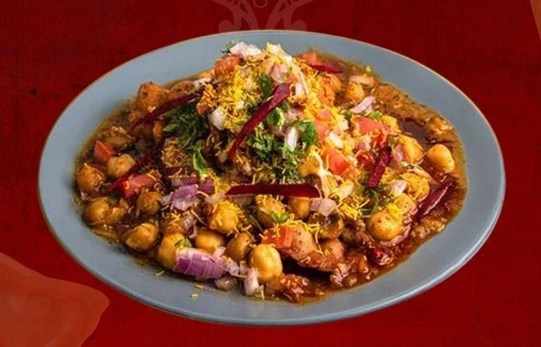 A plate of Indian chickpea curry garnished with chopped onions, tomatoes, herbs, and sliced red chili peppers.
