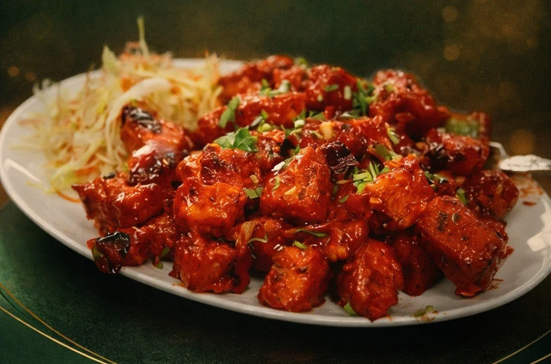 A plate of Asian-style spicy glazed chicken pieces garnished with chopped green onions, accompanied by shredded cabbage salad.