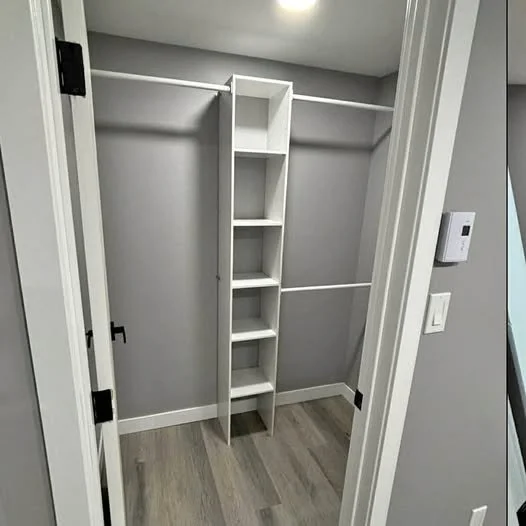 Empty walk-in closet with built-in shelves and horizontal hanging rods in gray walls and wood floor.
