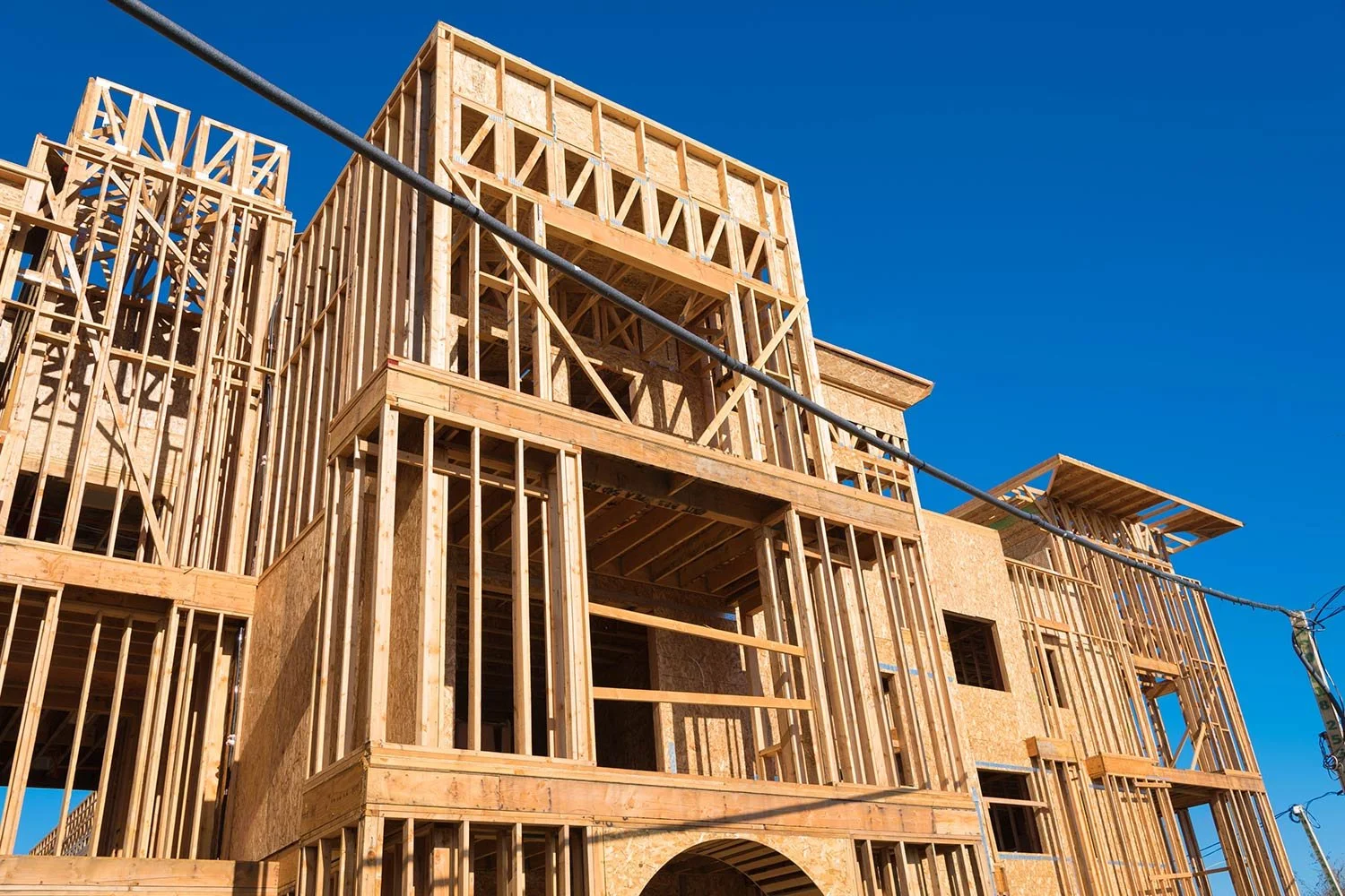 Wooden framing of a multi-story building under construction against a clear blue sky.