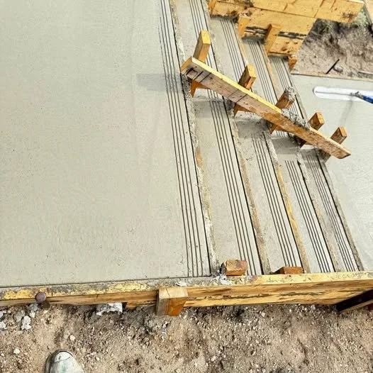A concrete floor with metal rebar grid, wooden formwork, and a wooden support beam at a construction site.