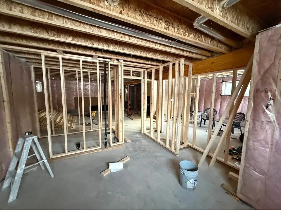 Construction of interior framing in a house, showing wooden studs and framework with drywall and insulation partially installed.
