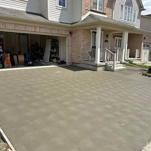 Newly poured concrete driveway in front of a two-story suburban house with a porch and garage, with some tools and materials inside the garage