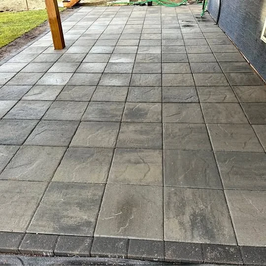 A newly paved grey brick patio area outside a house with a grassy patch on the left and a gray wall on the right.