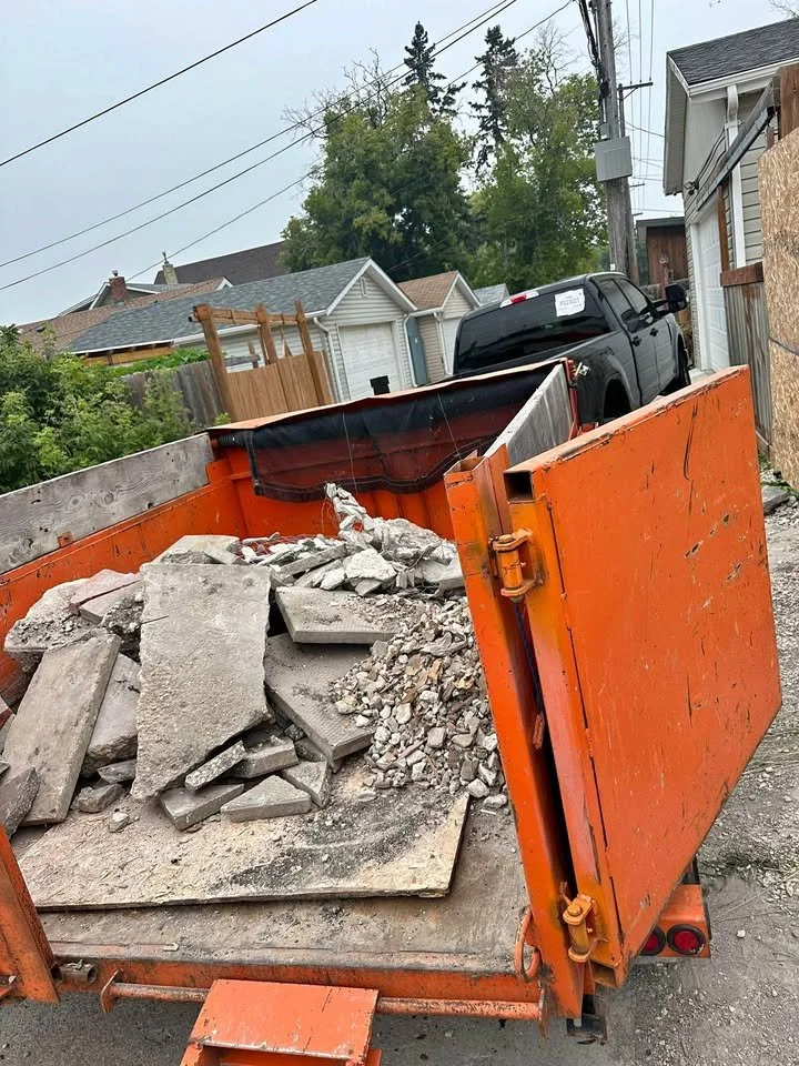 Dump truck filled with broken concrete and debris parked on a street in a residential neighborhood.