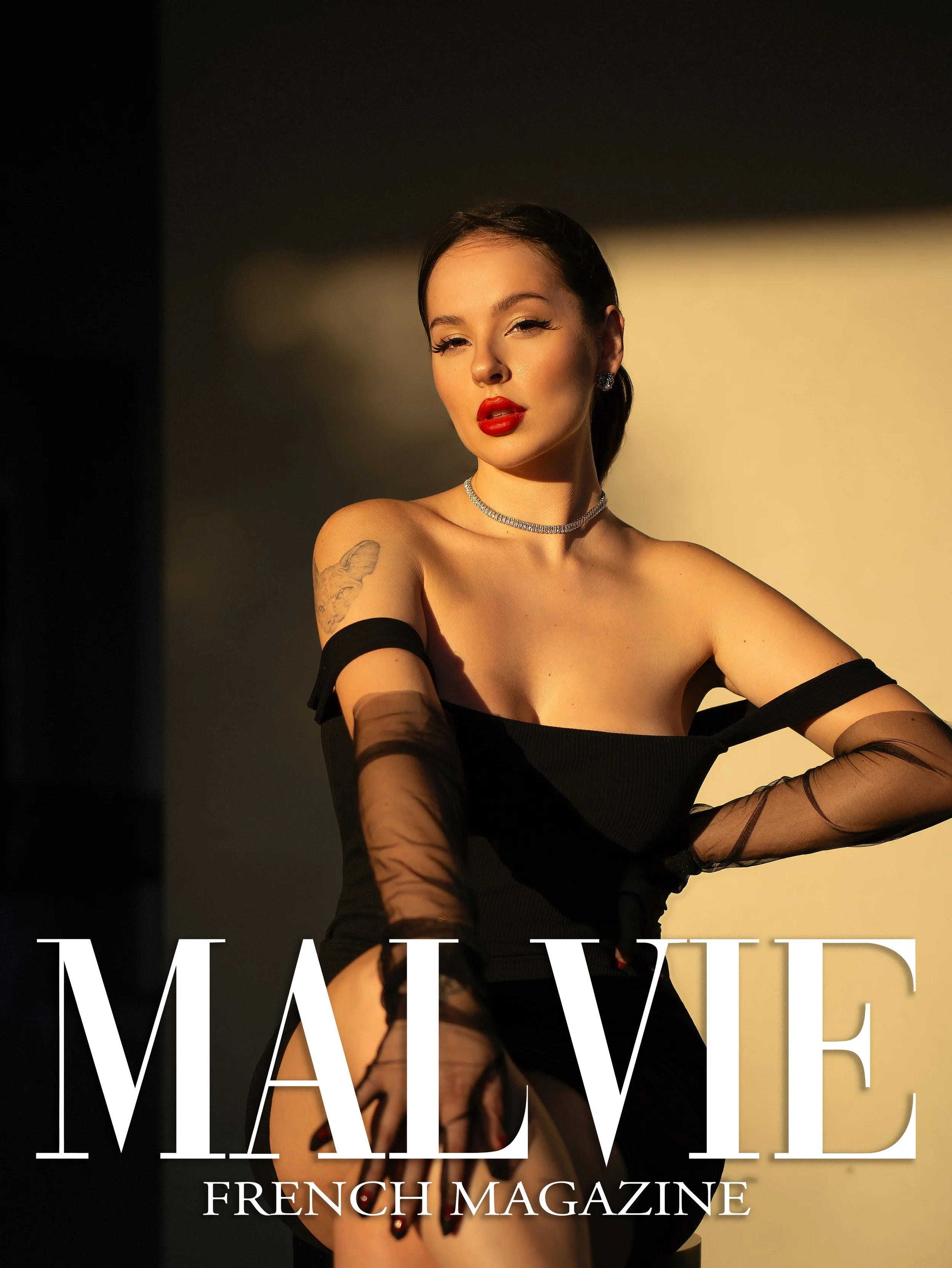 A woman with dark hair styled in a ponytail, wearing red lipstick, makeup, and jewelry, posing with one eye winking, dressed in black clothing with sheer gloves, magazine cover with large white text reading 'MADE' and smaller text 'FRENCH MAGAZINE'.