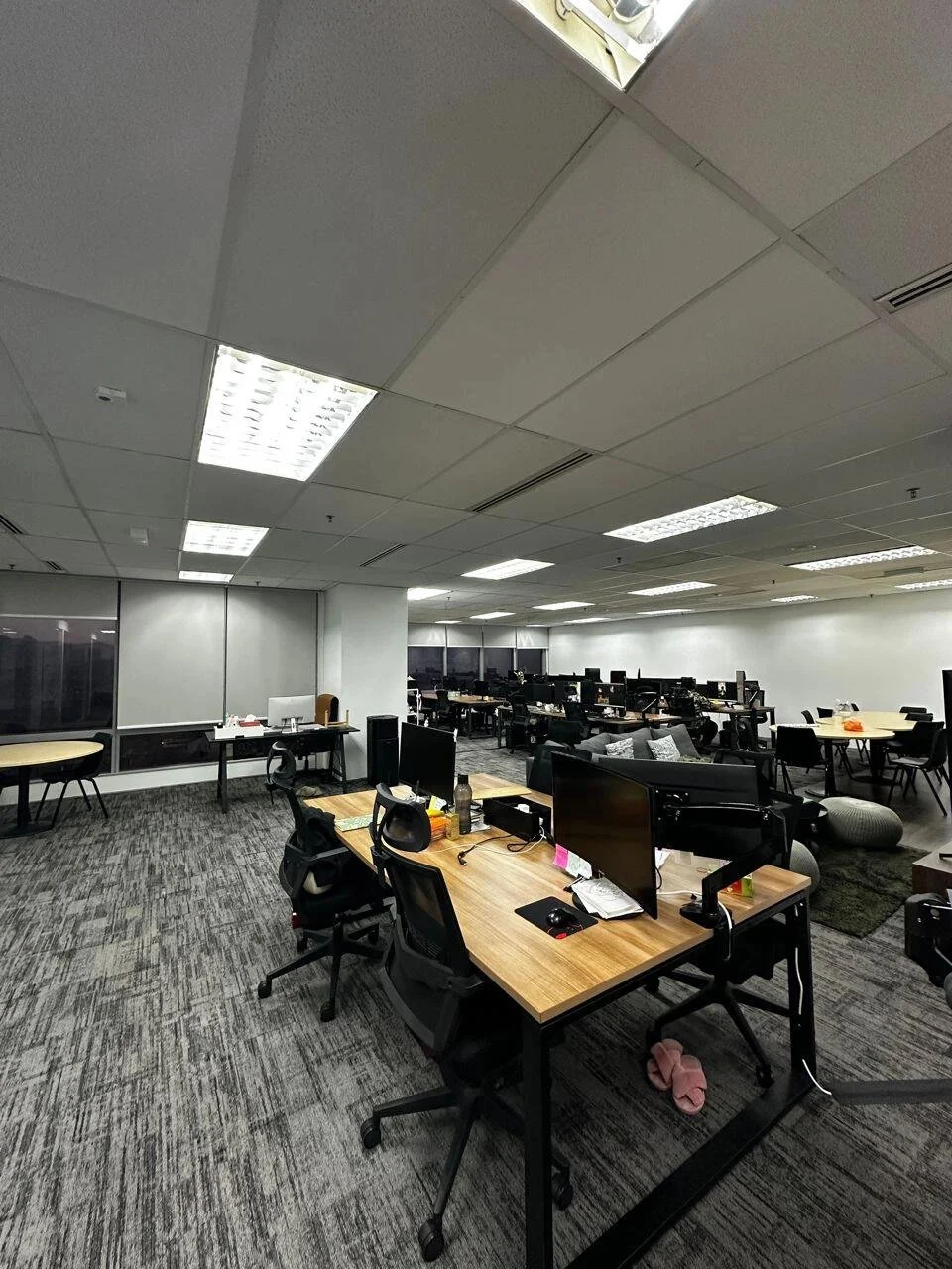 Empty office space with desks, chairs, computer monitors, and lighting fixtures on the ceiling.