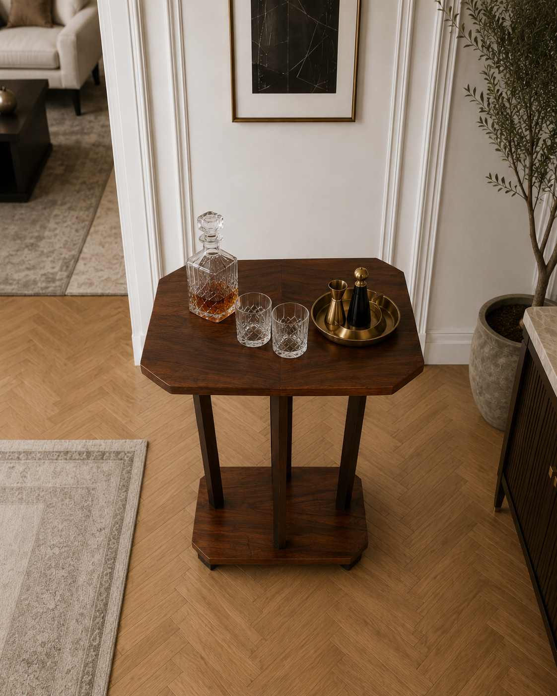 A wooden side table with a crystal decanter of whiskey, two matching whiskey glasses, and a gold tray with salt and pepper shakers in a modern living room.