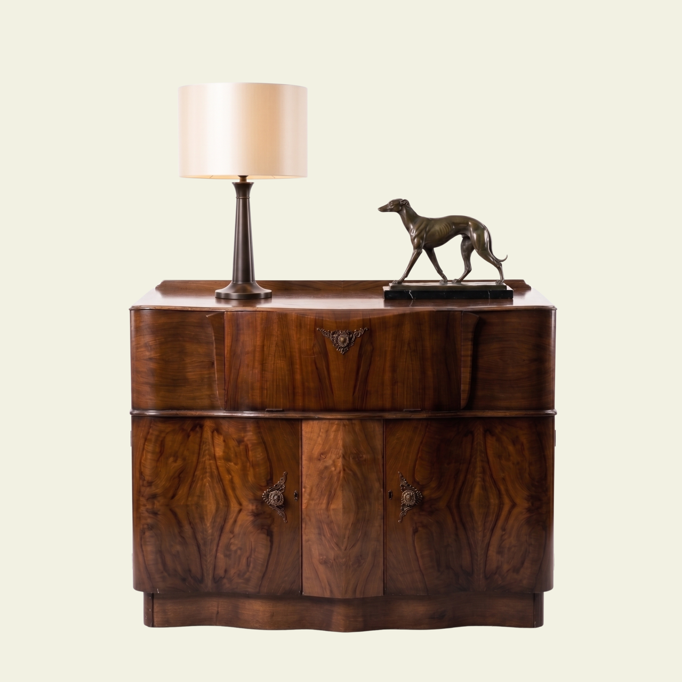 A wooden cabinet with decorative handles, a bronze-colored horse sculpture, and a table lamp with a cream lampshade and dark base.