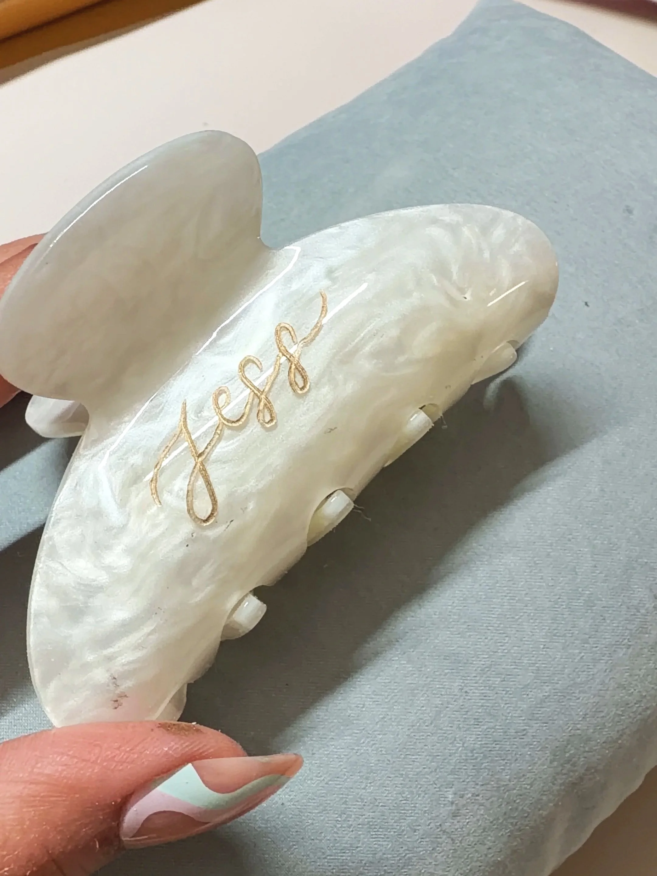 Close-up of a hand holding a carved white jade or stone piece with golden embroidery, resting on a light blue textured fabric.