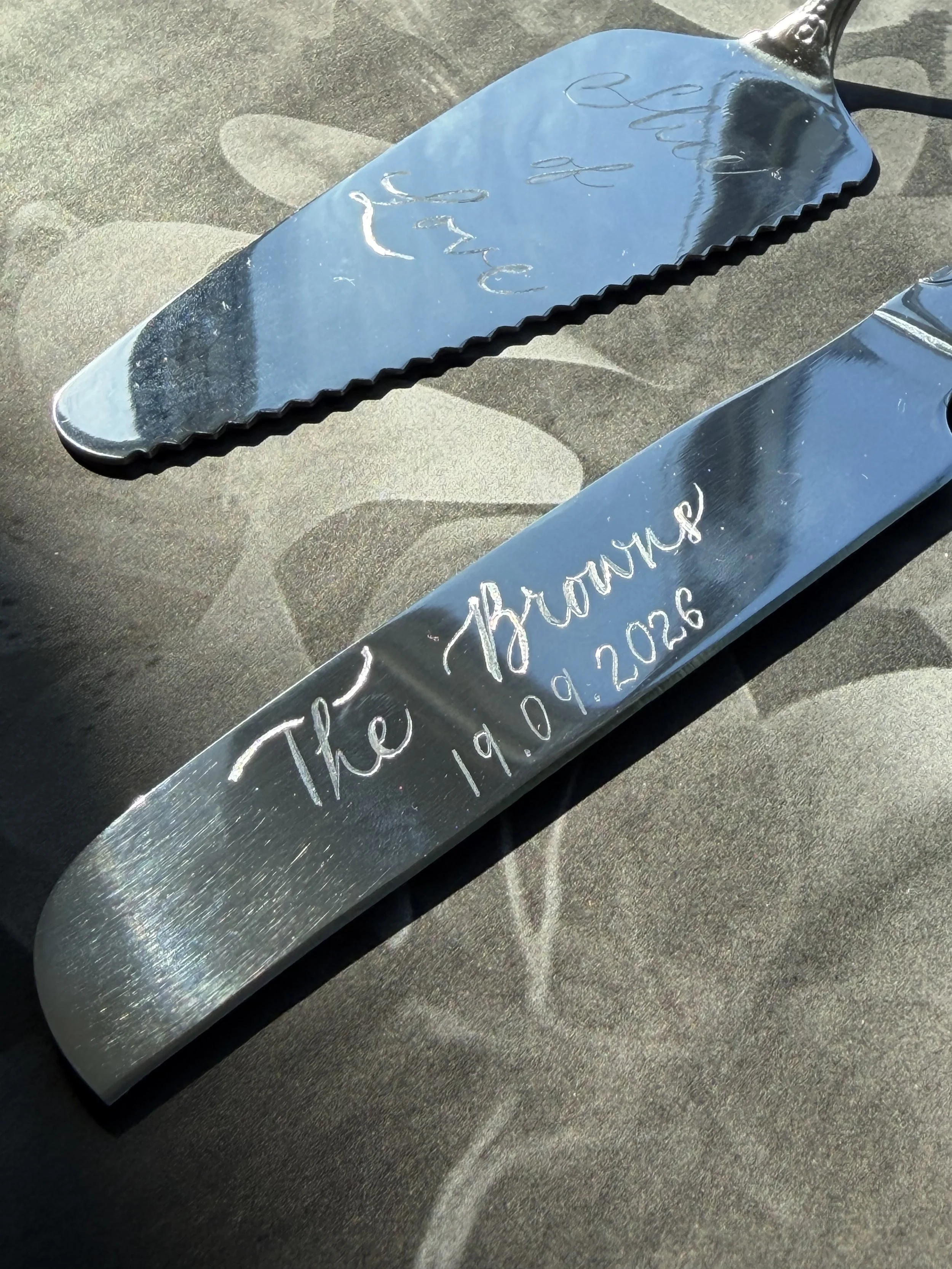 A rectangular mirror with a black handle, reflecting the sky and clouds, engraved with handwritten text and a date.