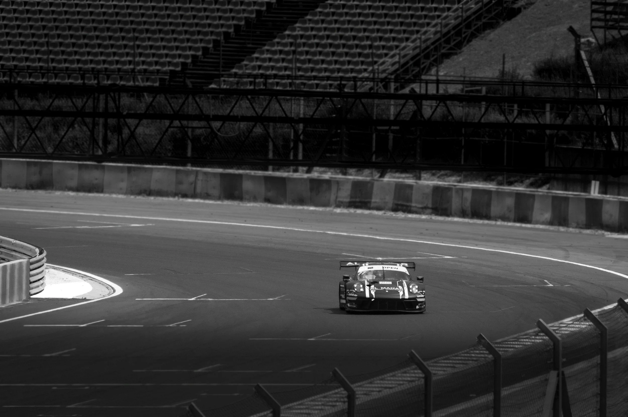 Black and white photo of a race car on a track with empty stands and safety barriers.