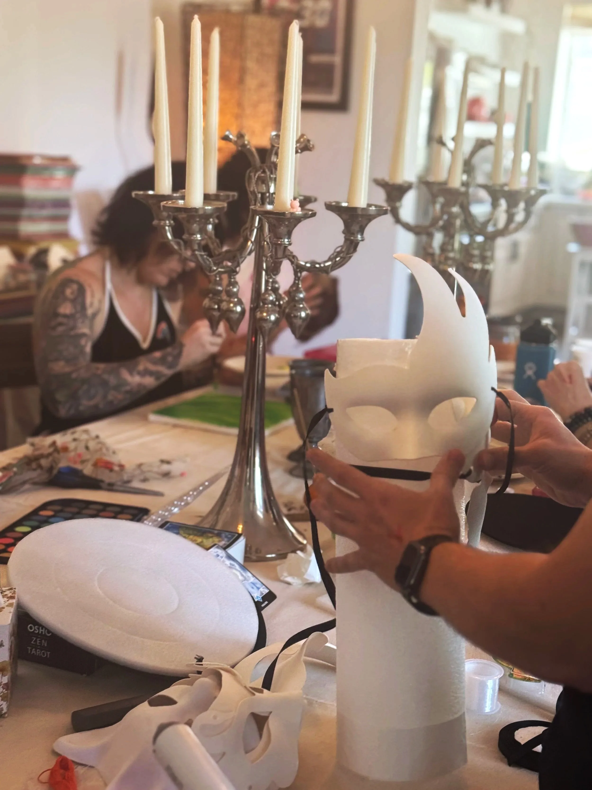 People working on arts and crafts project at a table, with candles and a skull-shaped object in the foreground during the creativity retreat Seducing the Muse.